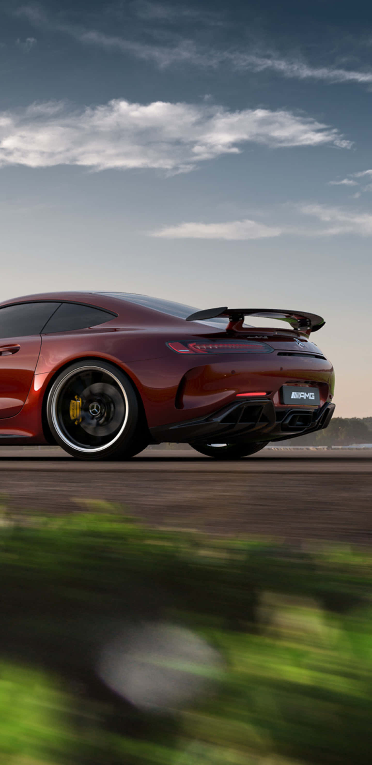 Red Car 桌布 壁紙 — 一輛酒紅色的 Mercedes-AMG GT R 跑車在道路上疾駛，背景是模糊的綠植和多雲的天空。