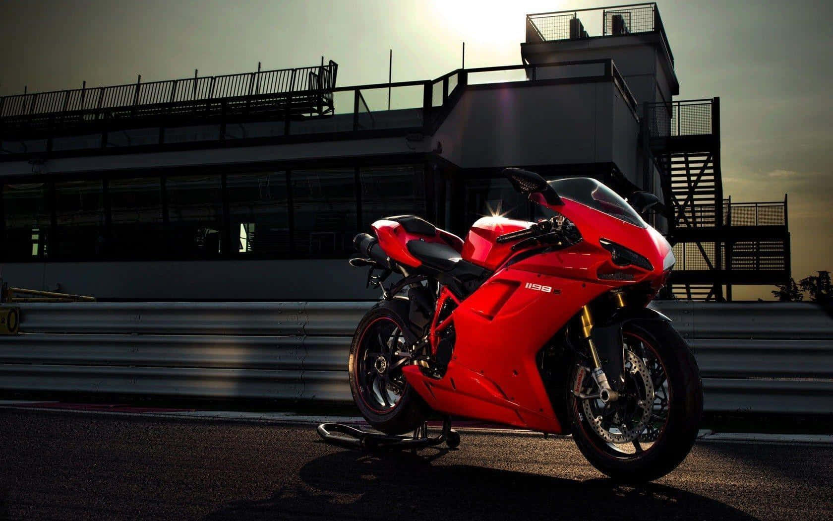 機車 桌布 壁紙 — 一輛醒目的紅色Ducati 1198摩托車在現代看台旁的賽道上，在金色夕陽下閃閃發光。