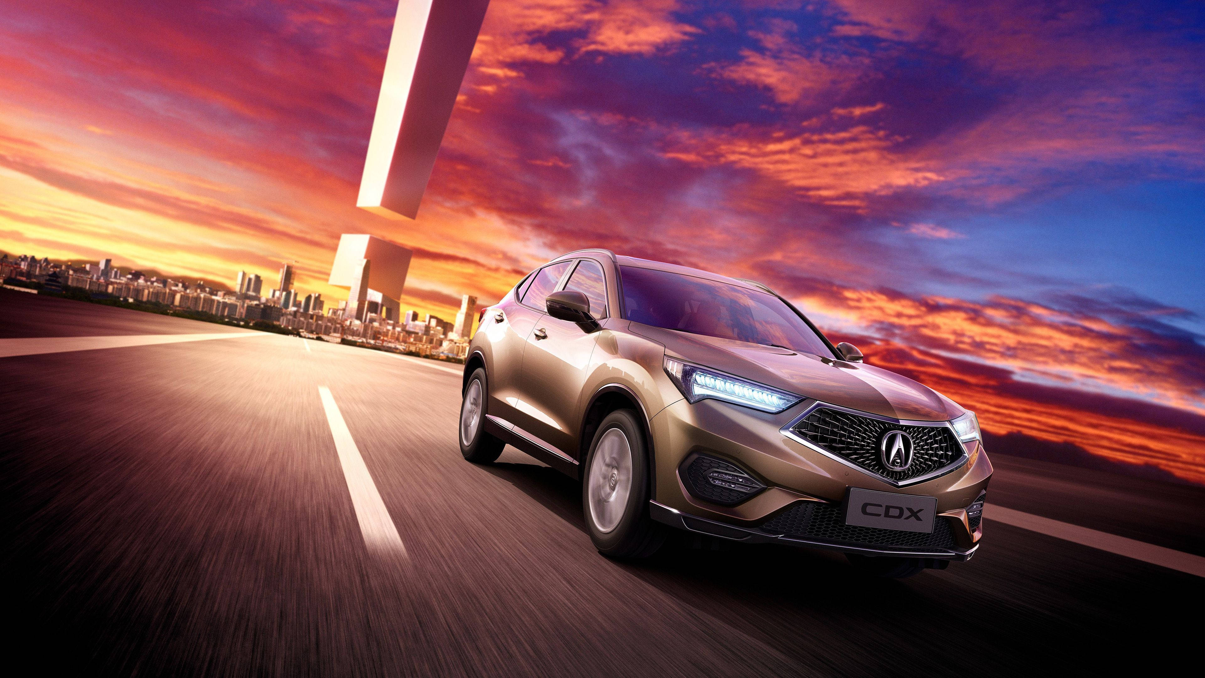 Acura 桌布 壁紙 — 一輛金色Acura CDX SUV在充滿活力的日落天空下高速行駛，遠處是未來主義的城市天際線。