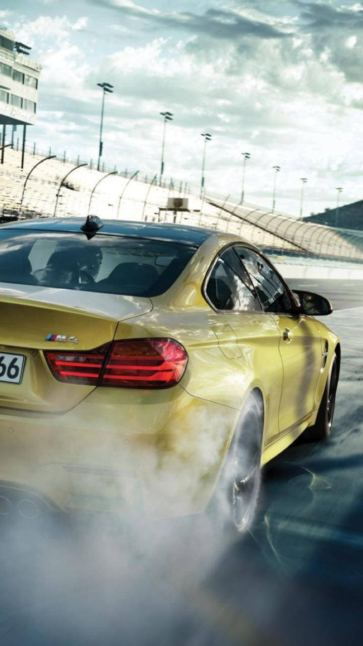 X 桌布 壁紙 — 一輛金色BMW M4在賽道上甩尾，在陰天下揚起煙霧。