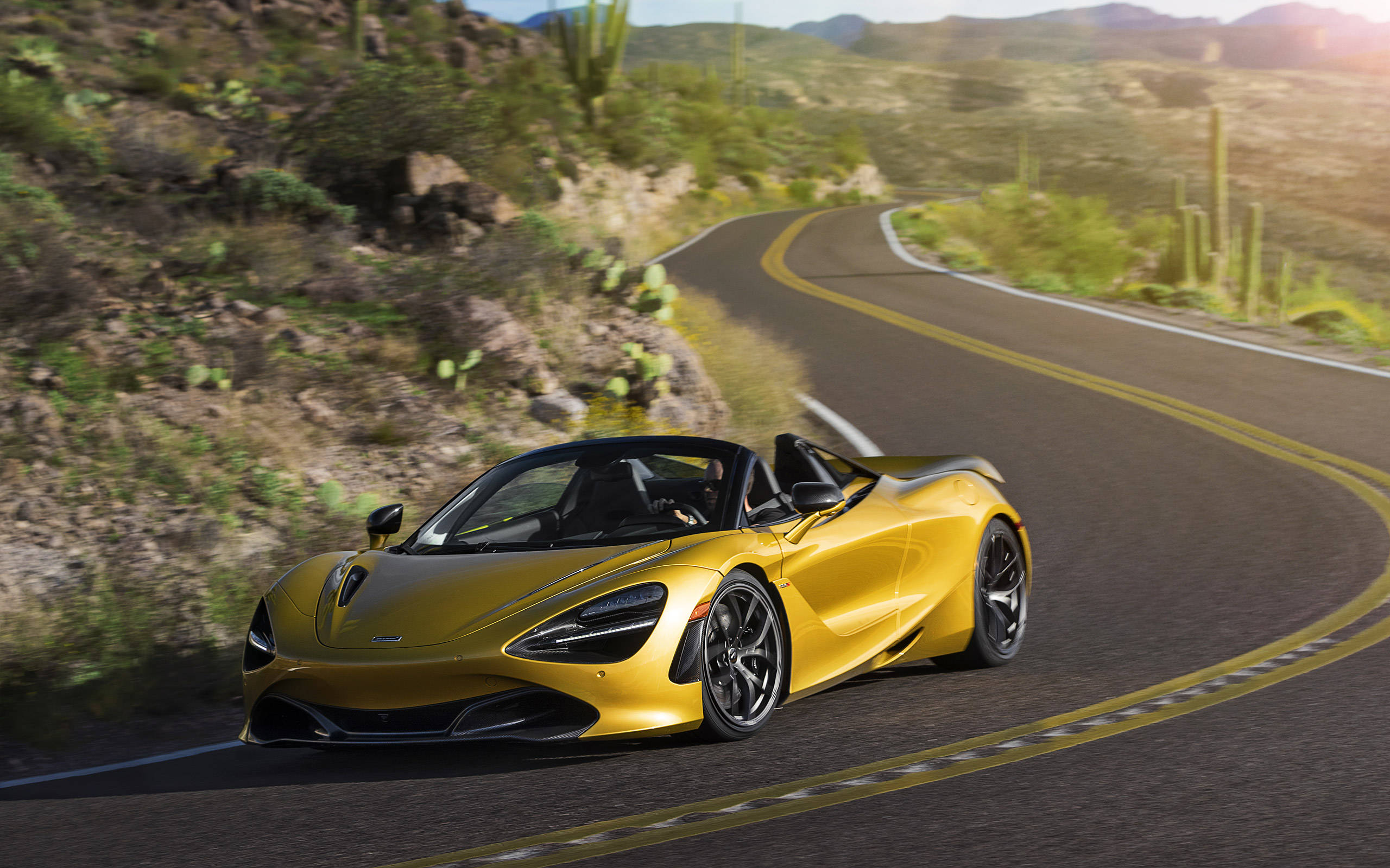 跑車 桌布 壁紙 — 一輛金色McLaren 720S Spider在陽光明媚下，沿著仙人掌叢生的蜿蜒沙漠公路飛馳。