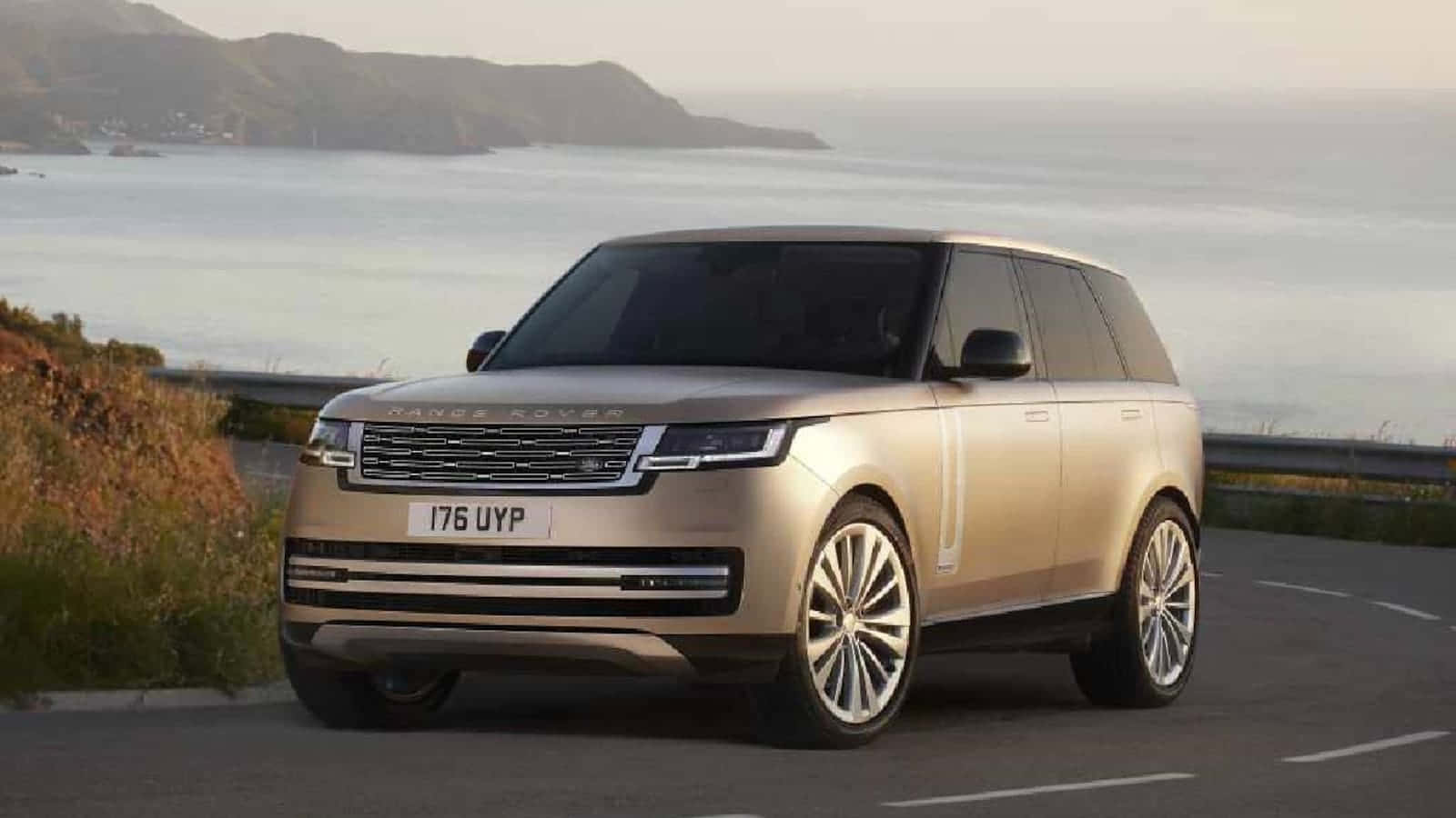 Range Rover 桌布 壁紙 — 一輛金色Range Rover SUV在黃金時段沿著海岸道路行駛，背景是山丘和海洋。