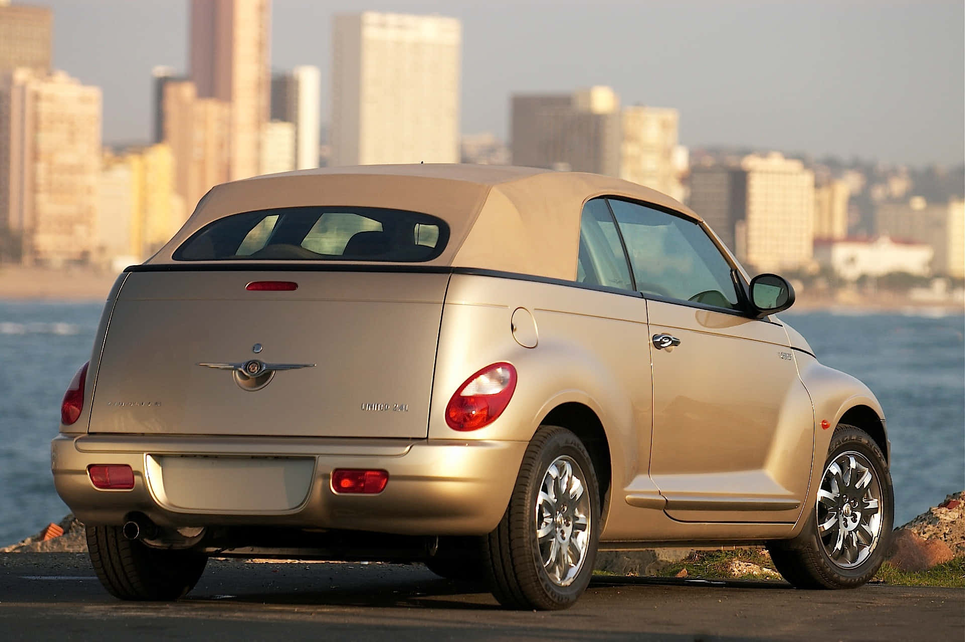 Chrysler Pt Cruiser 桌布 壁紙 — 一輛金色克萊斯勒 PT Cruiser 敞篷車停在水邊，背景是城市天際線。