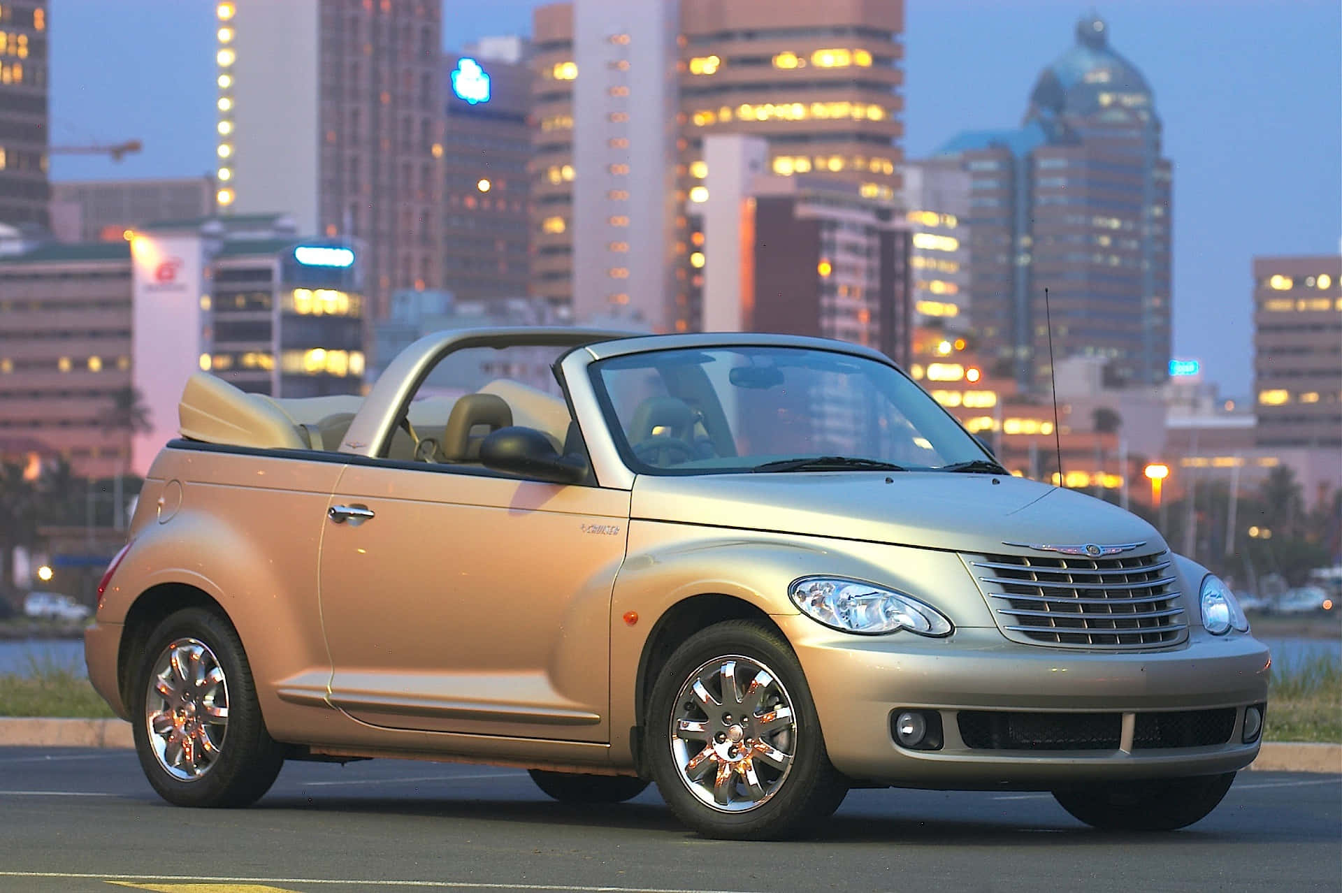 Chrysler Pt Cruiser 桌布 壁紙 — 一輛金色克萊斯勒PT Cruiser敞篷車在黃昏時停泊在城市的街道上，背景是燈火通明的摩天大樓。