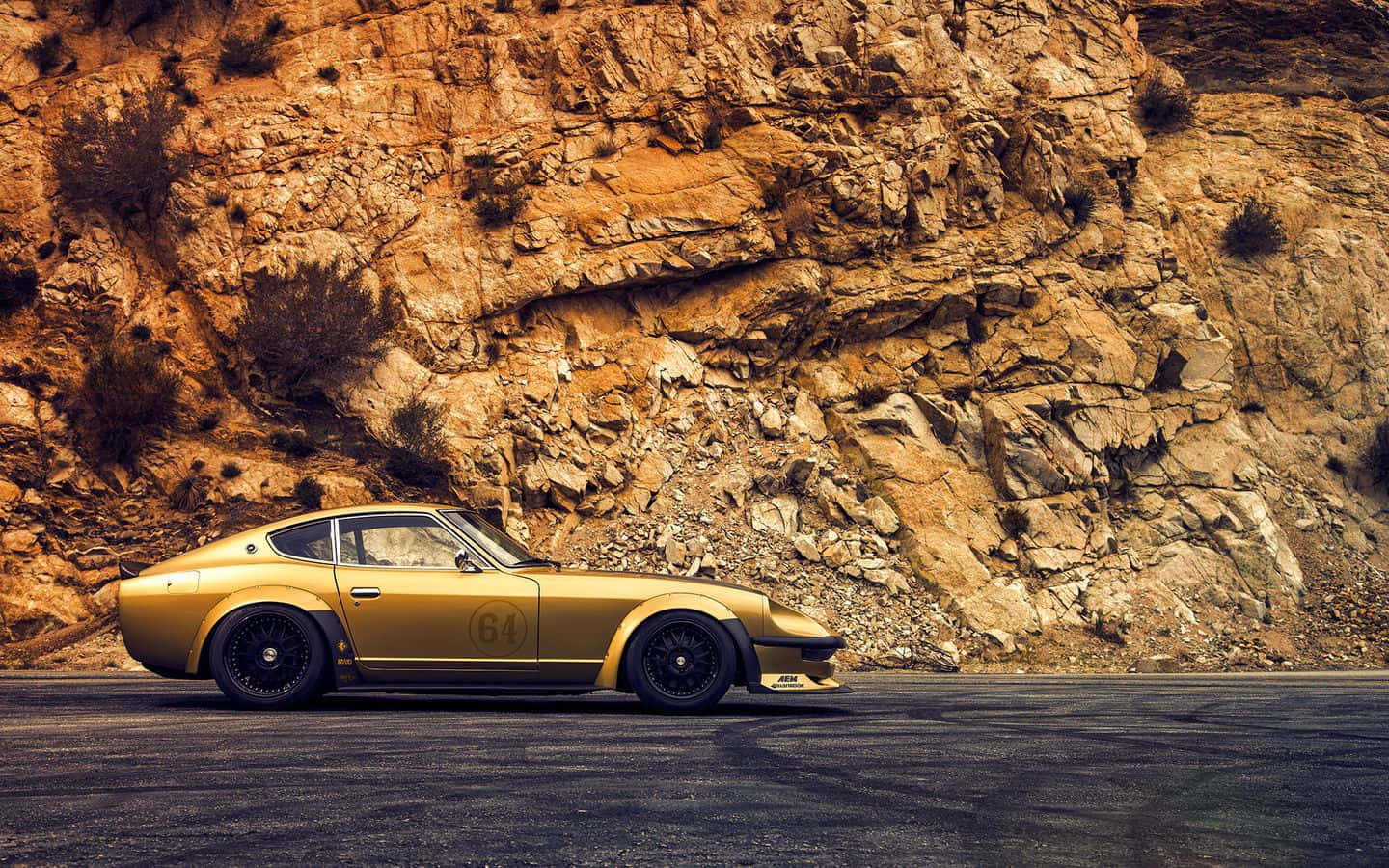 Datsun 桌布 壁紙 — 一輛金色復古賽車，編號64，停泊在蜿蜒的道路上，背景是崎嶇的岩石懸崖。