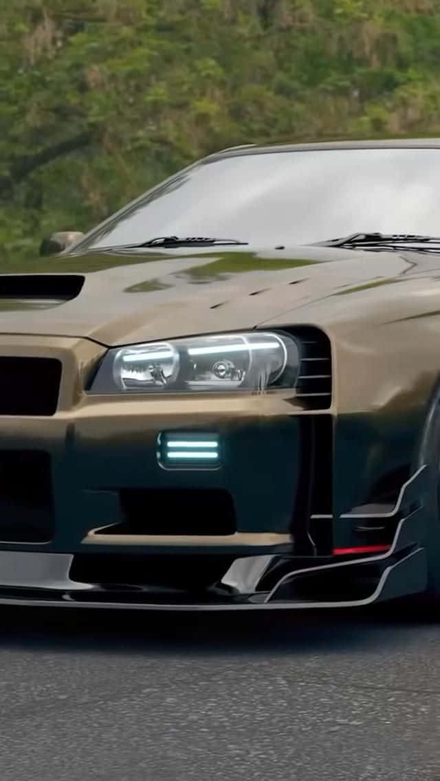 日產 桌布 壁紙 — 一輛金色日產GT-R，帶有發光藍色飾邊和黑色空氣動力部件，停在瀝青路面上，背景有綠色樹葉。