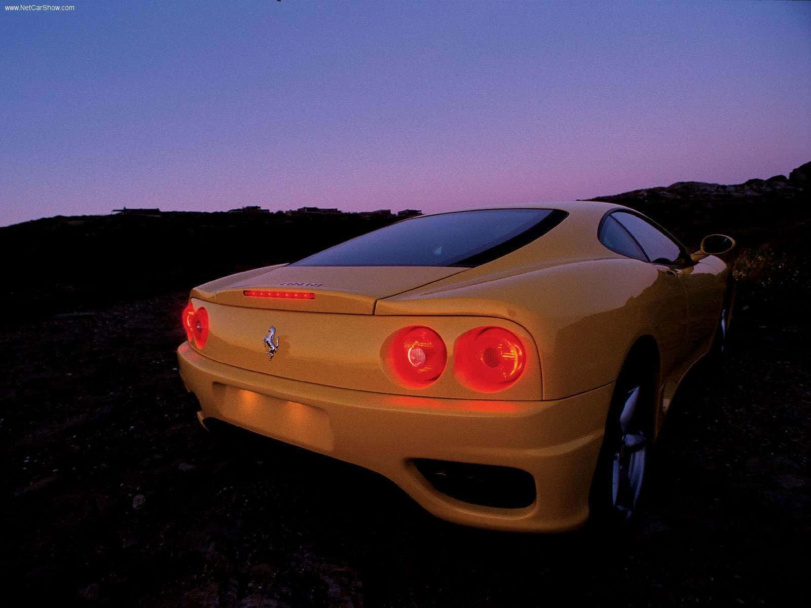 Ferrari 360 Modena 桌布 壁紙 — 一輛金色法拉利360跑車在岩石地形上，尾燈發出紅光，映襯著暮色天空。