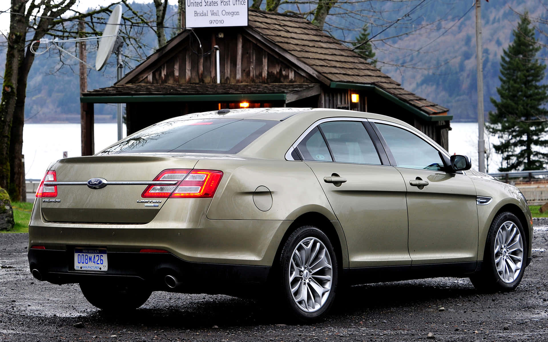 Ford Taurus 桌布 壁紙 — 一輛金色福特 Taurus 房車停在湖邊鄉村郵局前，背景有山巒。