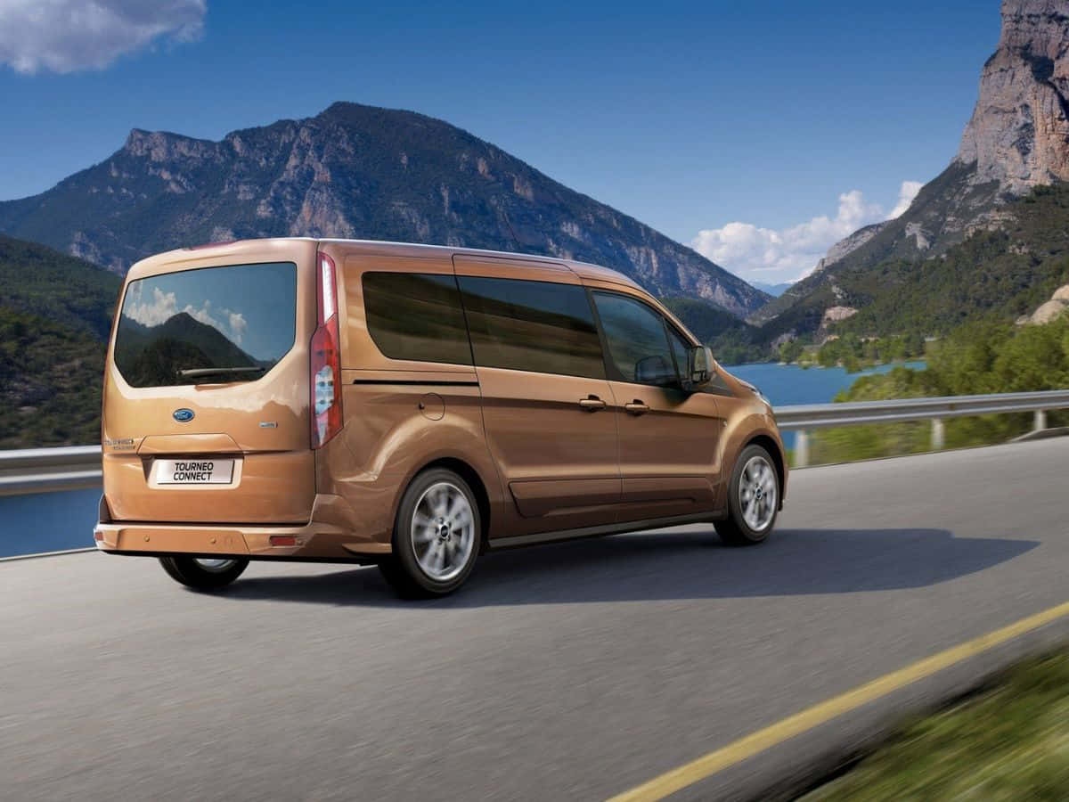 Ford Transit 桌布 壁紙 — 一輛金色福特 Tourneo Connect 客貨車在晴朗的藍天下沿著湖邊的山路行駛。
