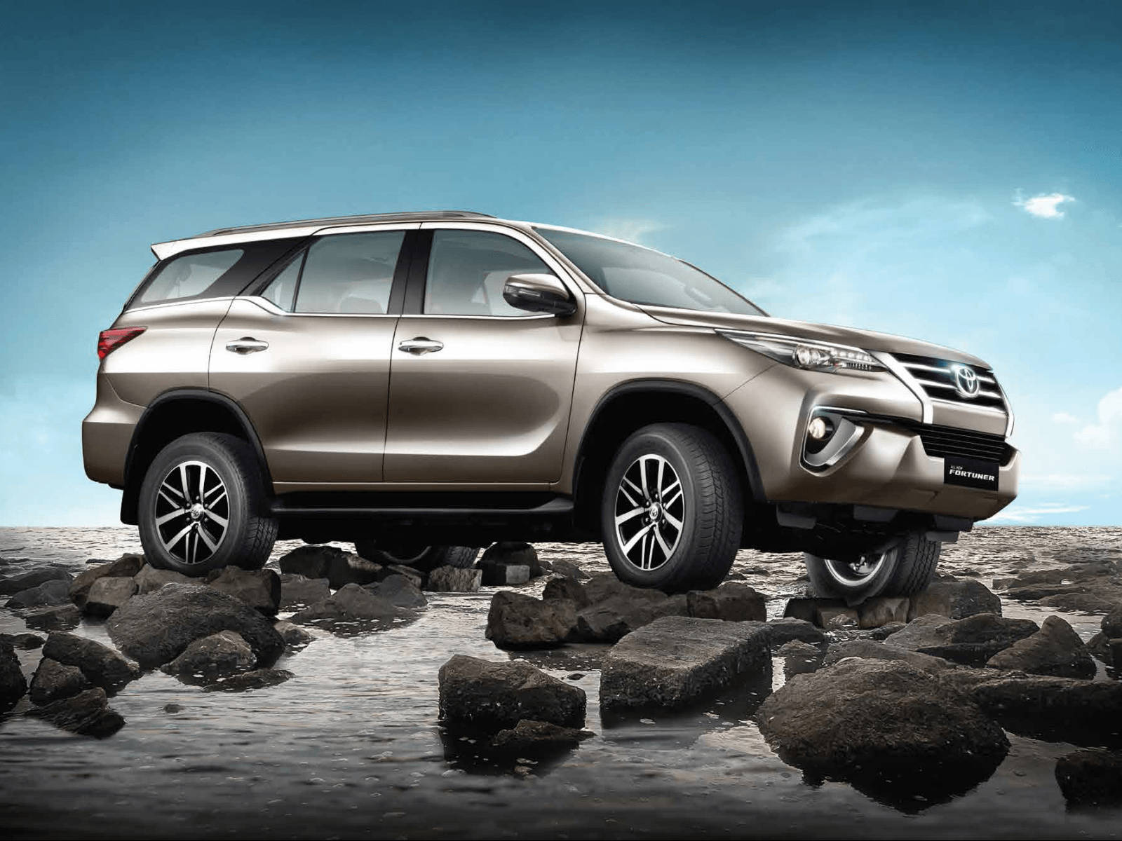 金色豐田 Fortuner SUV 在藍天下於淺水中行駛在濕岩石上。 — Toyota Supra Mk4 壁紙