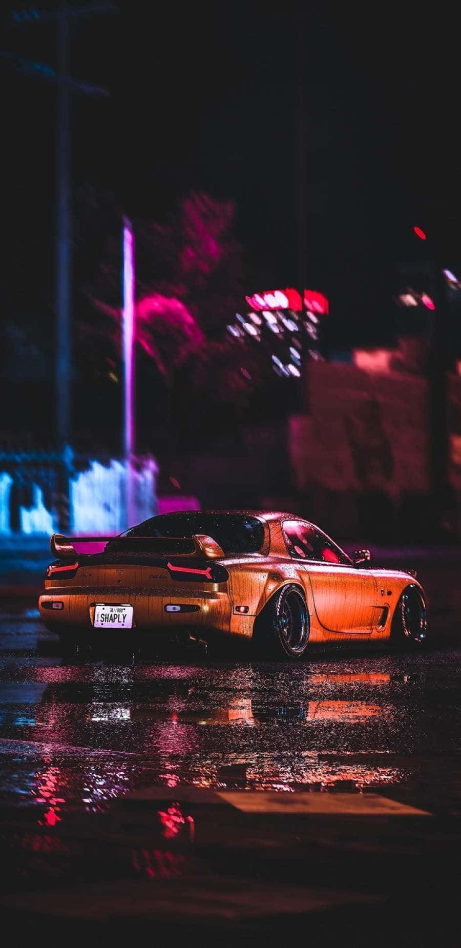 JDM 桌布 壁紙 — 一輛金色跑車在夜晚濕漉漉的城市街道上閃閃發光，在黑暗天空下的水坑中反射出霓虹燈光。