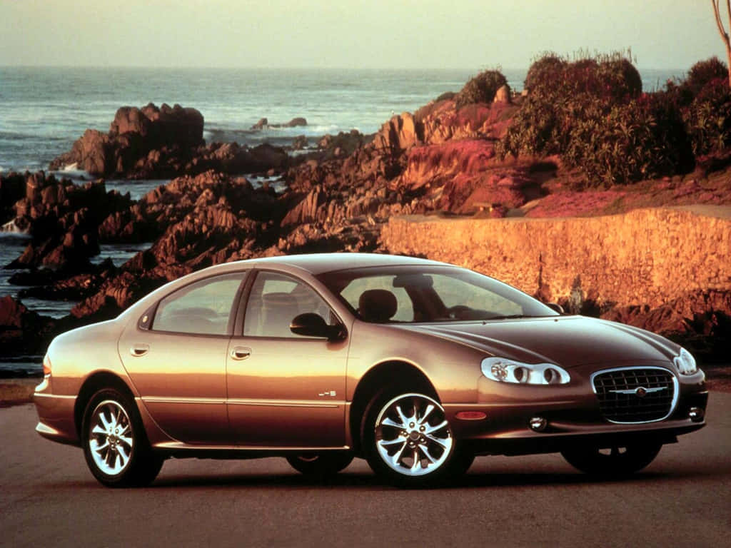 Chrysler Lhs 桌布 壁紙 — 一輛金色轎車停泊在沿海道路上，背景是岩石懸崖和日落時分的海浪。