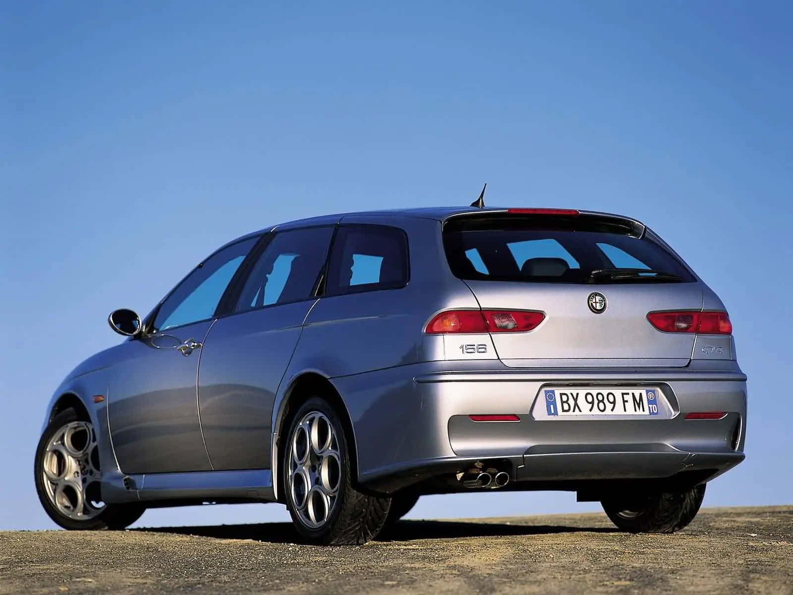 Alfa Romeo 156 桌布 壁紙 — 一輛銀色 Alfa Romeo 156 旅行車停泊在碎石平原上，天空清澈湛藍。