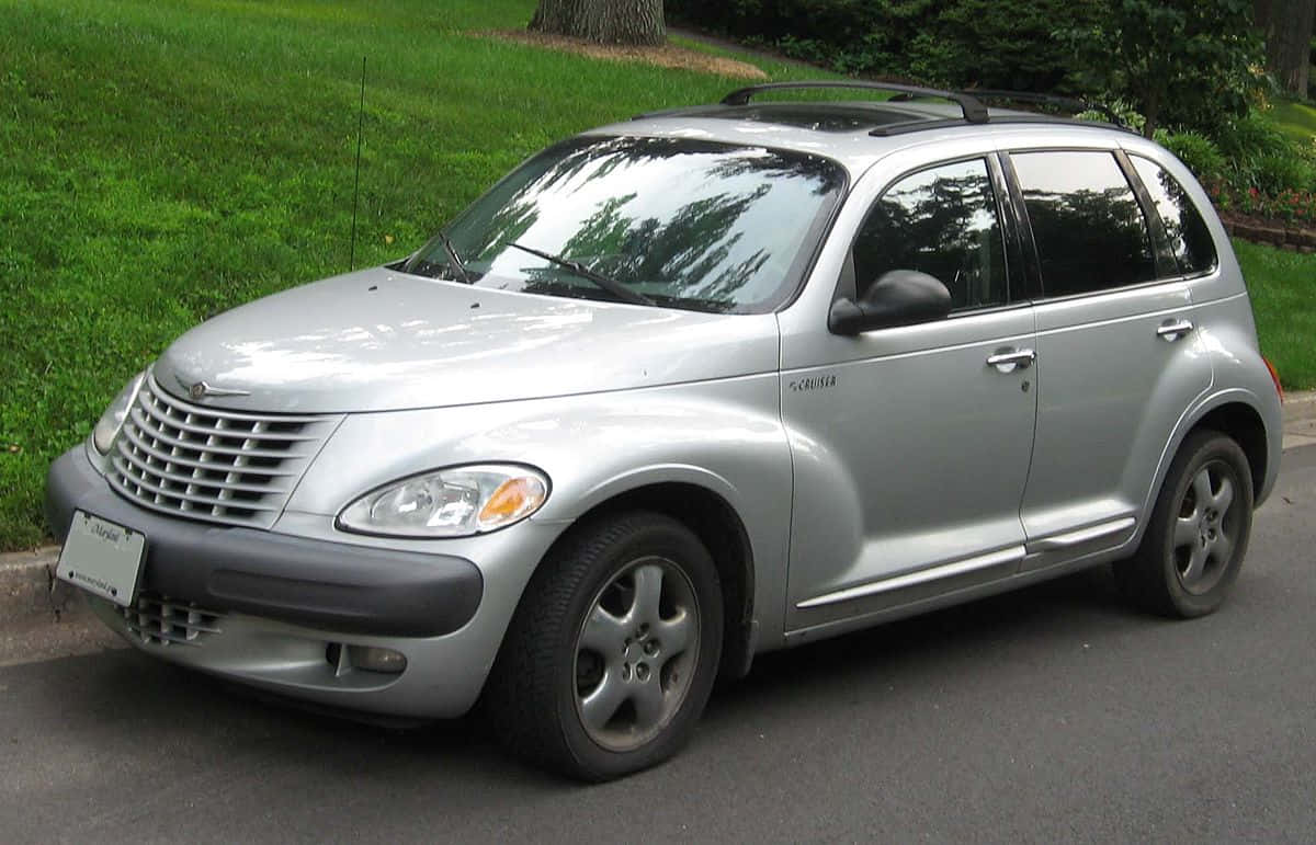 Chrysler Pt Cruiser 桌布 壁紙 — 一輛銀色 Chrysler PT Cruiser 在明亮日光下停放在街道上，旁邊是翠綠茂盛的草坪。