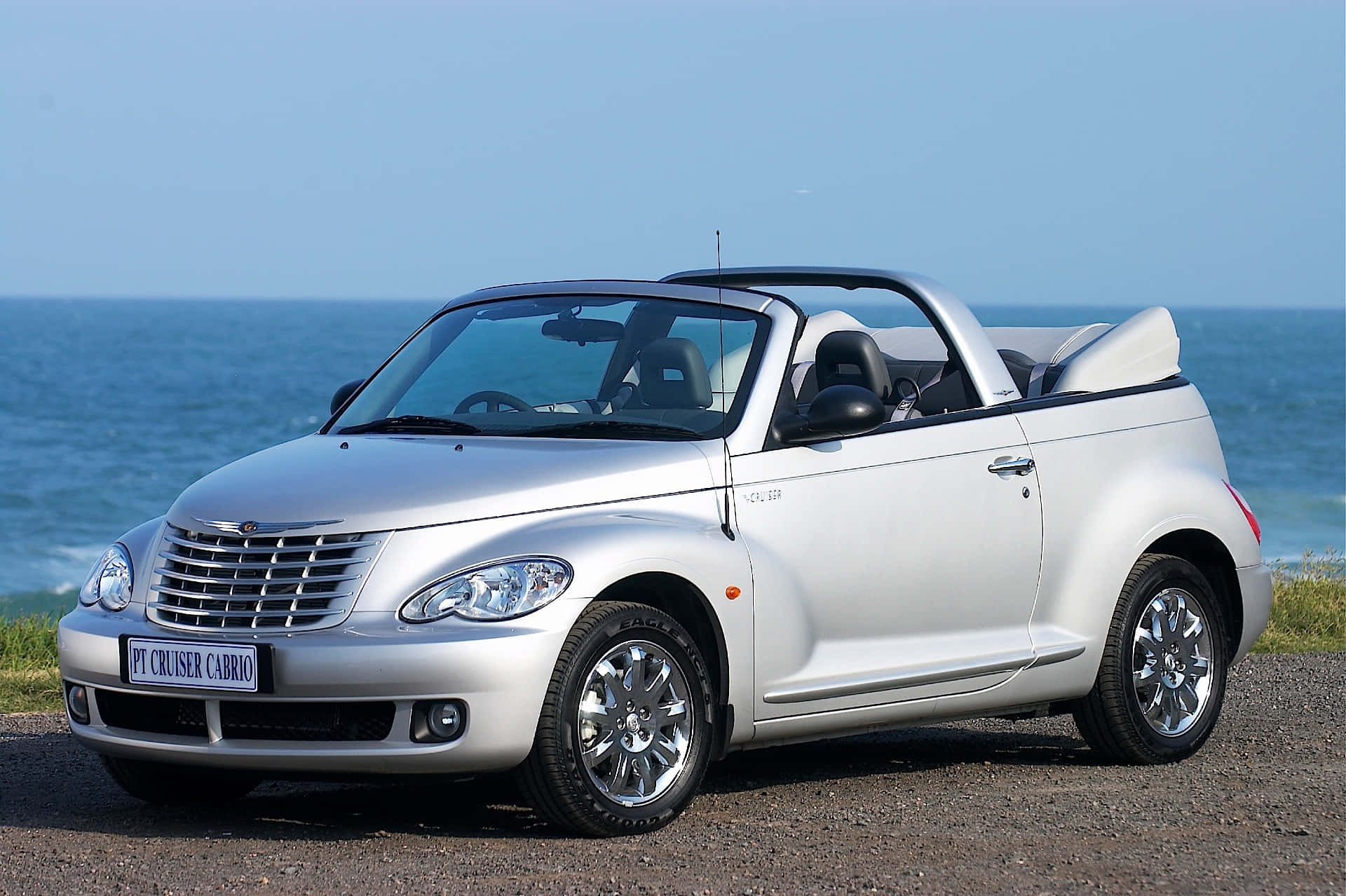 Chrysler Pt Cruiser 桌布 壁紙 — 一輛銀色 Chrysler PT Cruiser Cabrio 敞篷車停在碎石海灘上，背景是海洋和晴朗的天空。