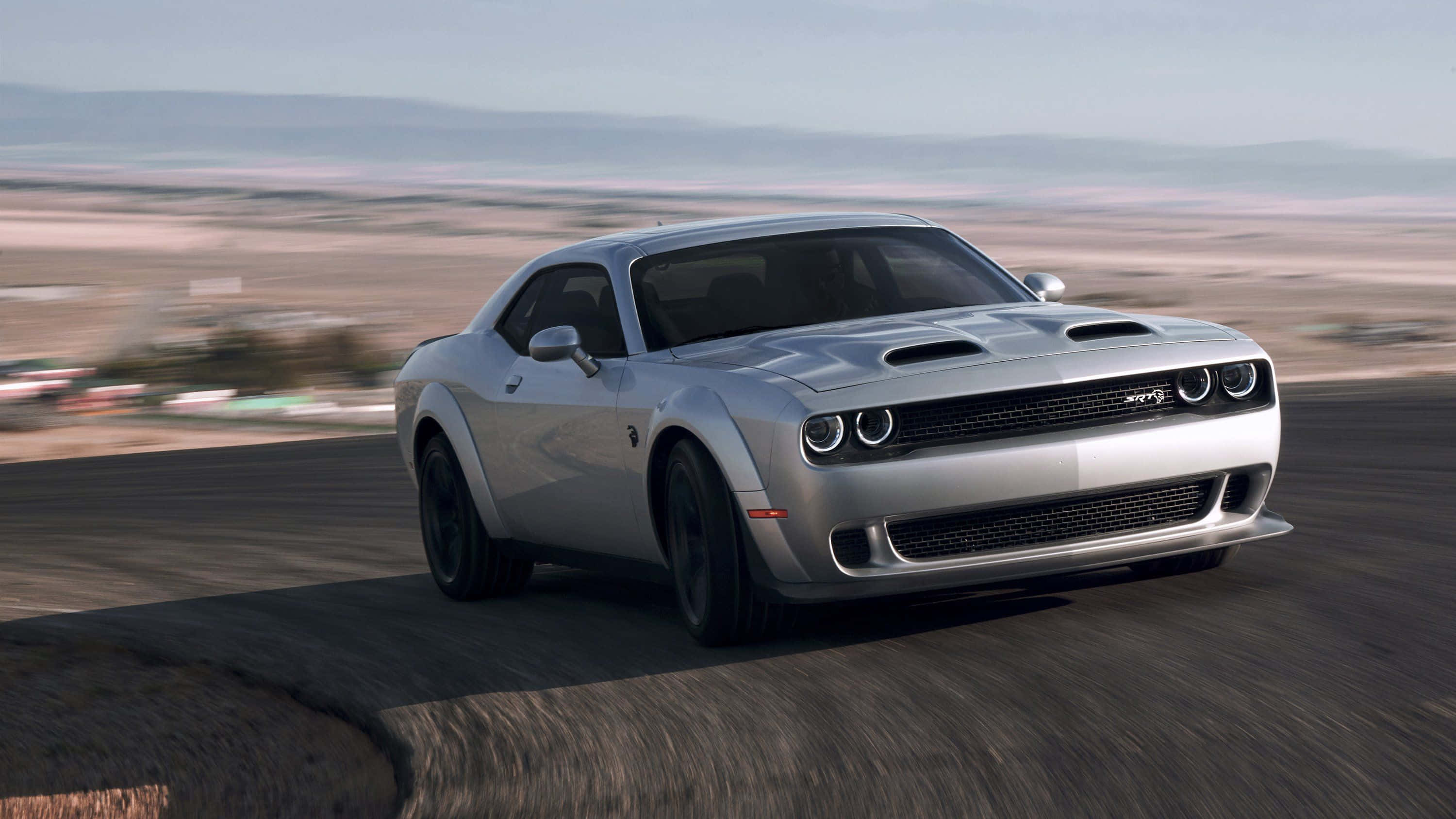 汽車 4K 桌布 壁紙 — 一輛銀色 Dodge Challenger SRT Hellcat 在沙漠公路上疾馳，背景模糊。