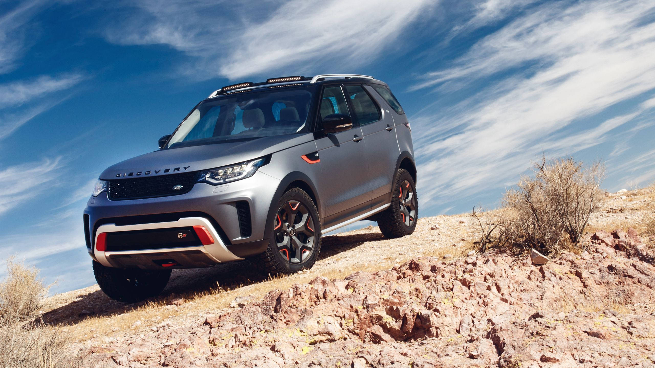 荒原路華 桌布 壁紙 — 一輛銀色 Land Rover Discovery 在藍天白雲下征服岩石沙漠斜坡。