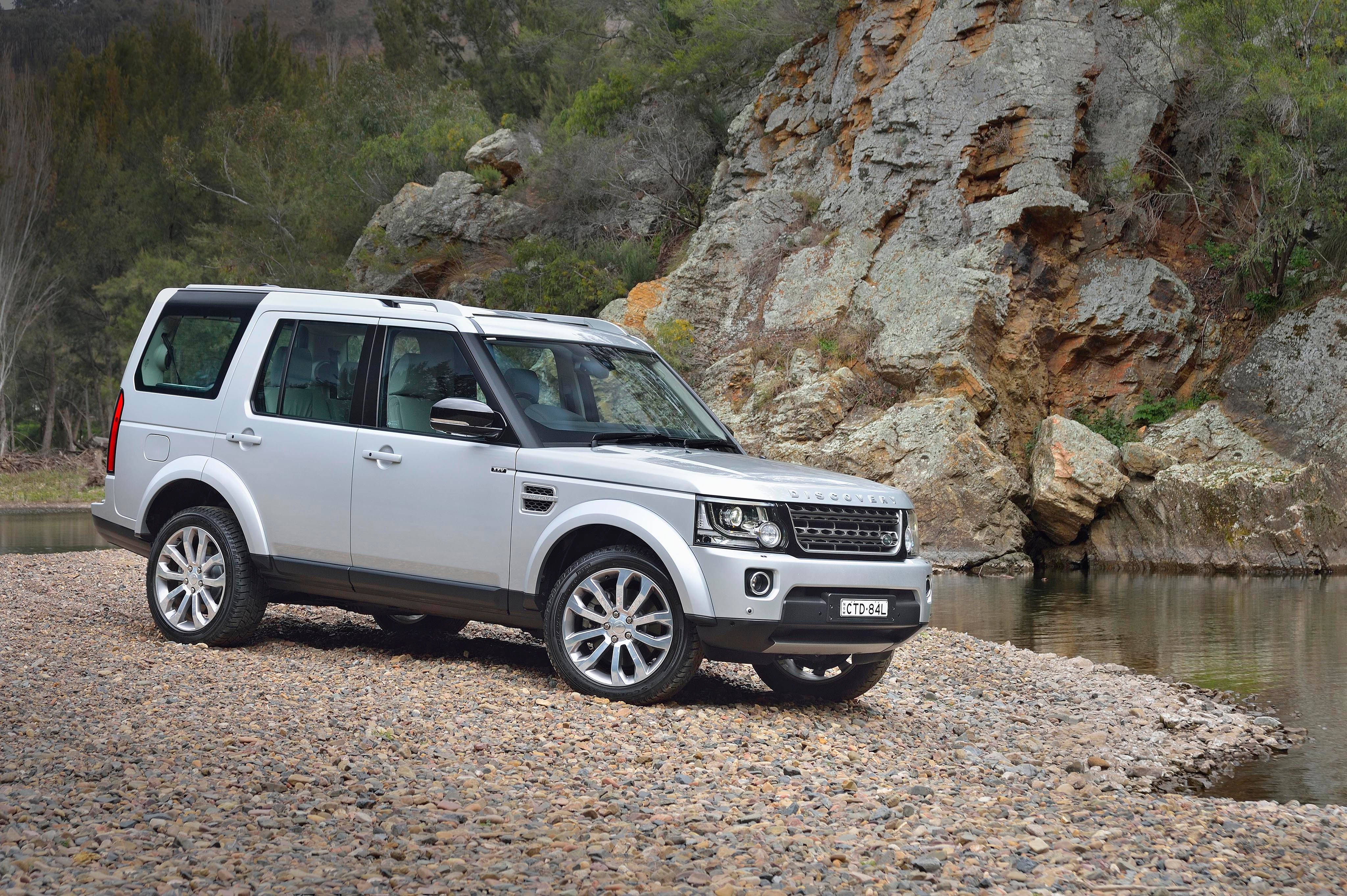 A 桌布 壁紙 — 一輛銀色 Land Rover Discovery 停泊在鵝卵石河岸旁，旁邊有崎嶇的懸崖和綠樹。