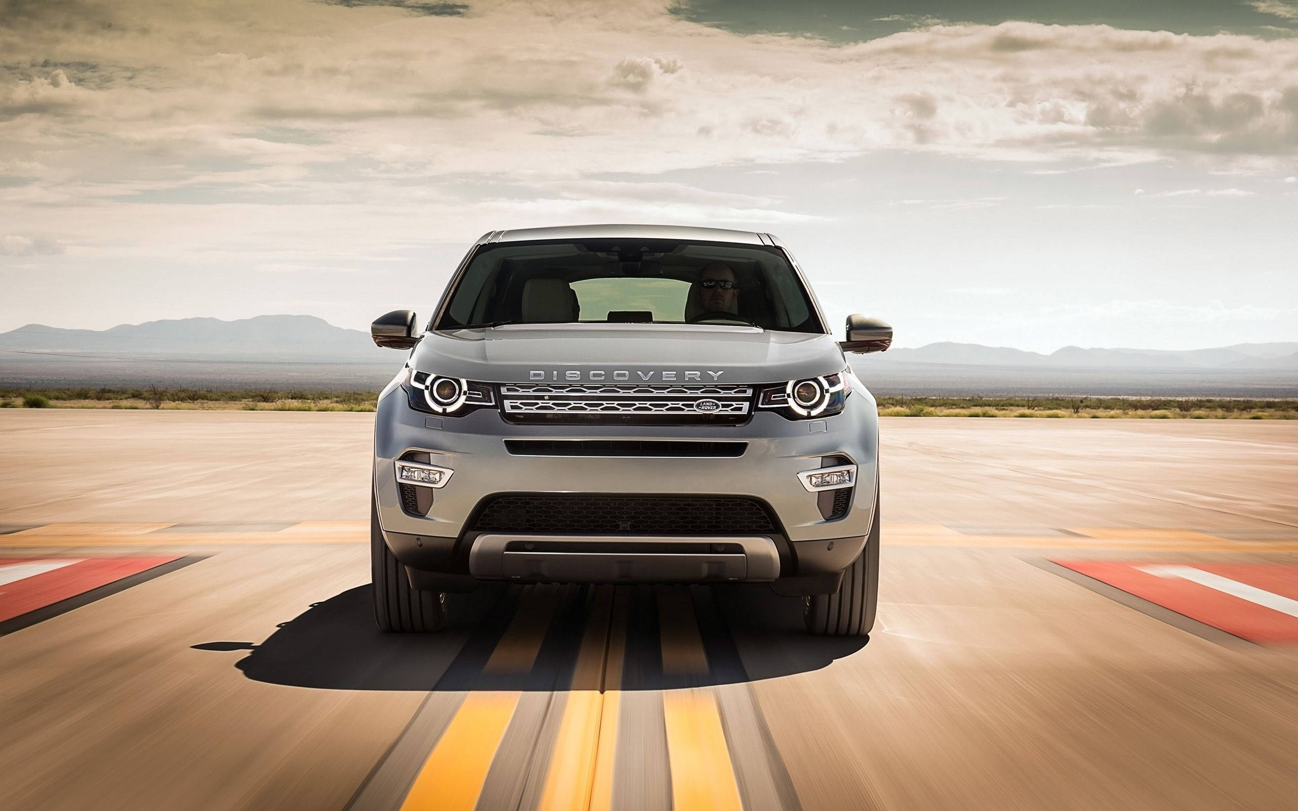 荒原路華 桌布 壁紙 — 一輛銀色 Land Rover Discovery 在沙漠賽道上疾馳，帶有模糊的運動線條，天空多雲。