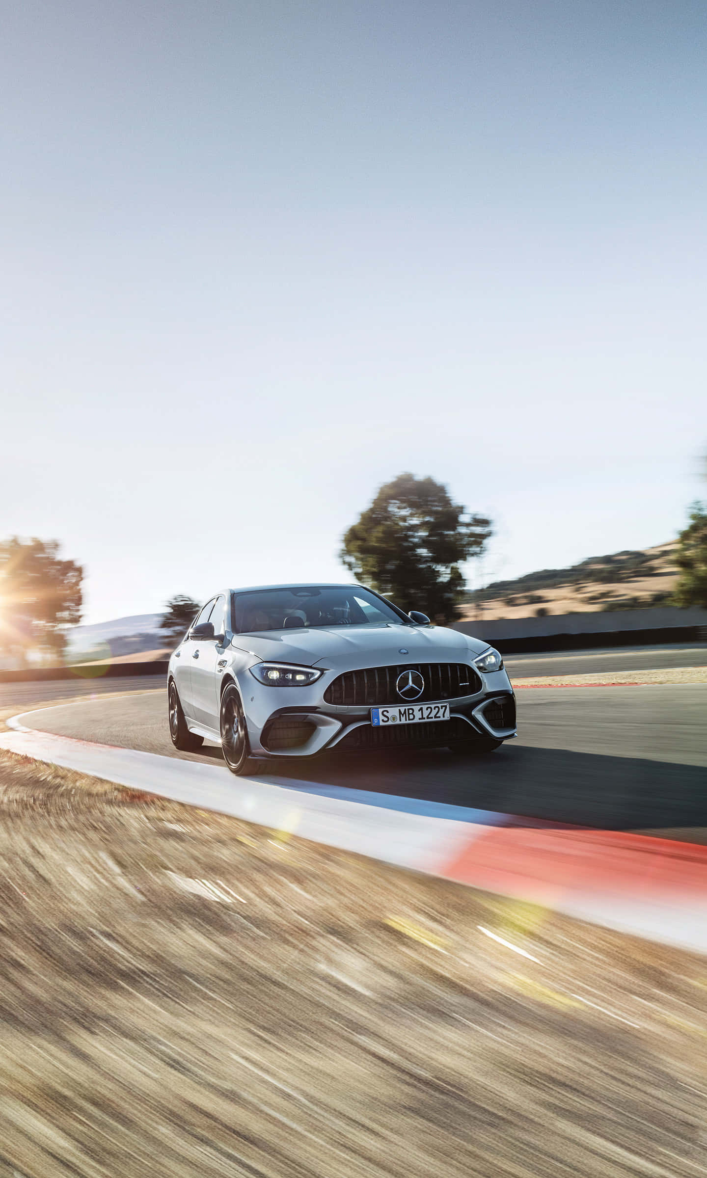 桌布 壁紙 — 一輛銀色 Mercedes-AMG 跑車在陽光普照的賽道上疾馳，帶有動態模糊和紅白路緣。