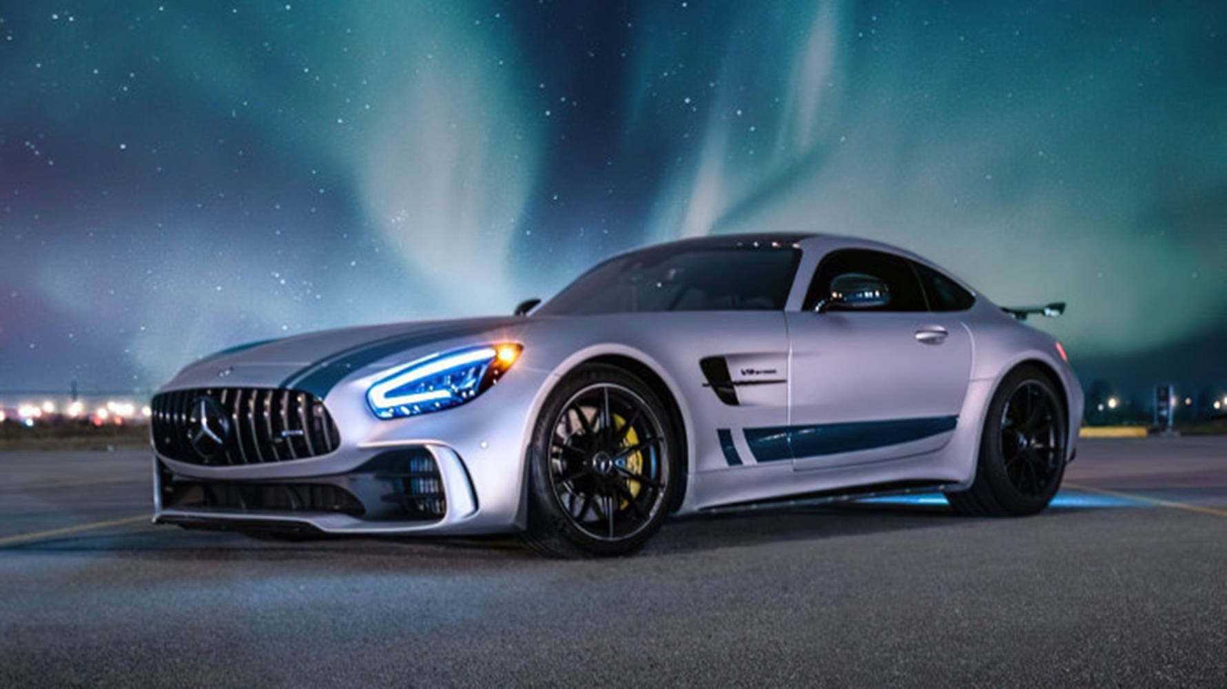 aurora borealis 桌布 壁紙 — 一輛銀色 Mercedes-AMG GT 停泊在停機坪上，上方是充滿活力的綠色北極光和繁星點點的夜空。