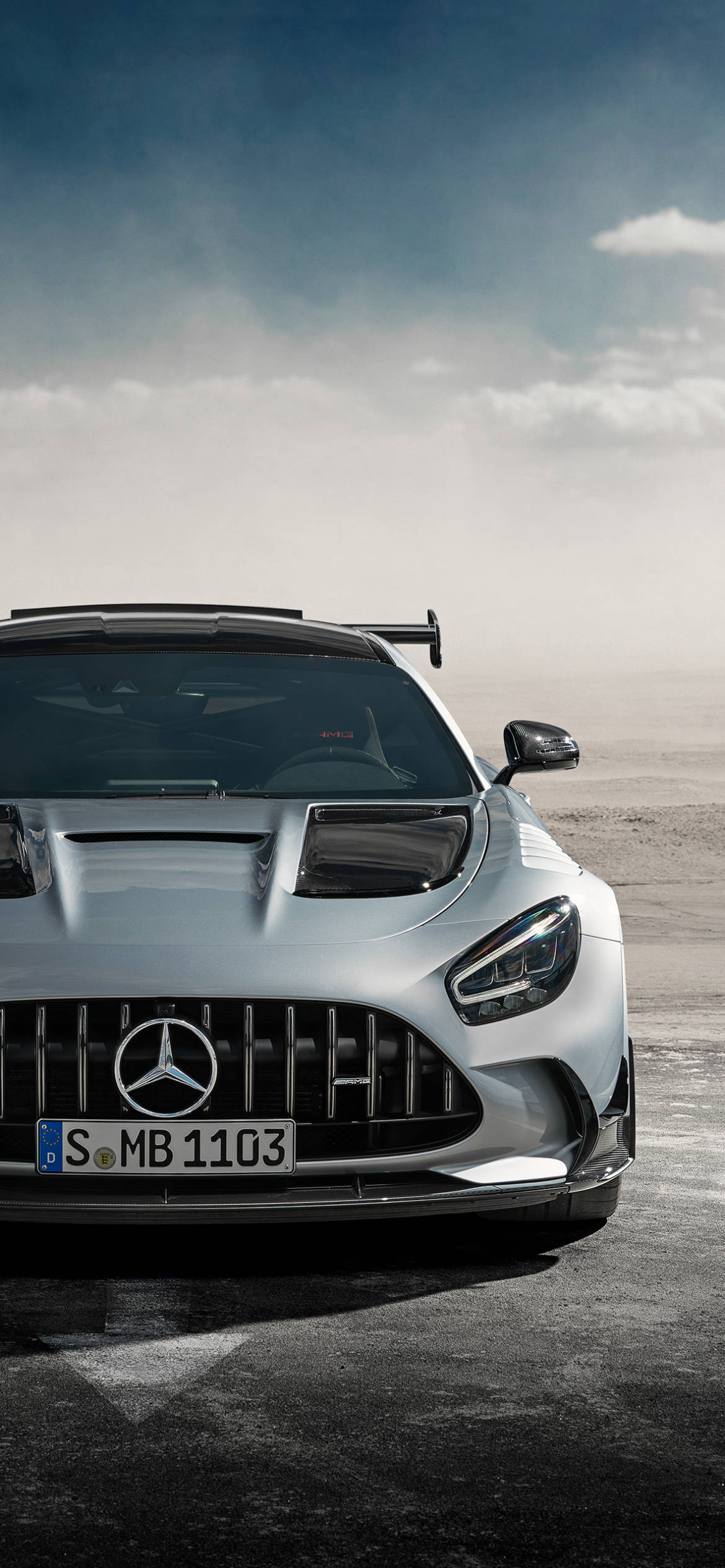 mercedes amg iPhone 桌布 壁紙 — 一輛銀色 Mercedes-AMG GT R 賽車在陰天的塵土賽道上蓄勢待發。