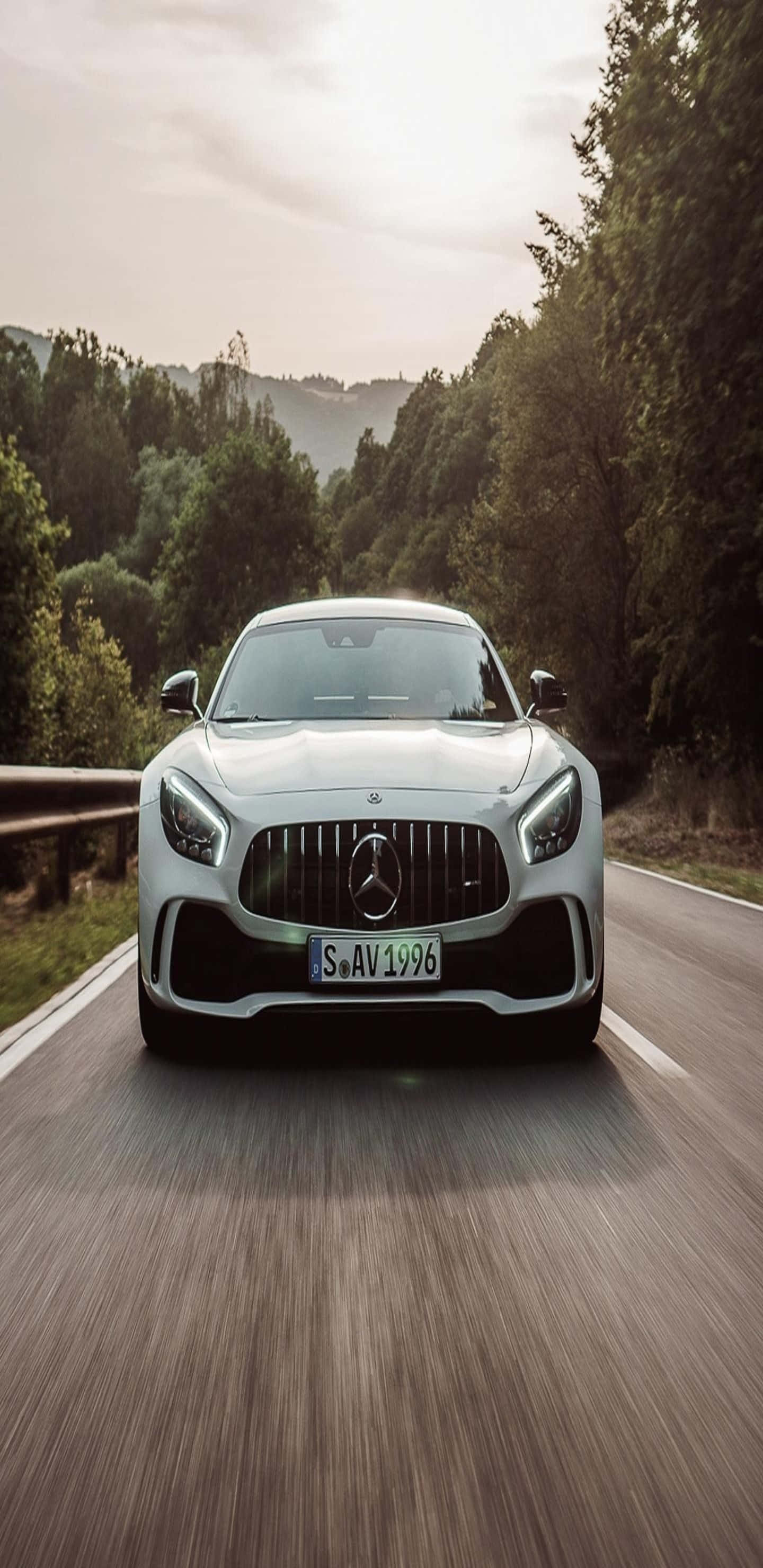 Car Phone 桌布 壁紙 — 一輛銀色 Mercedes-AMG GT 在蜿蜒的林間道路上疾馳，帶有動態模糊和柔和的金色光線。