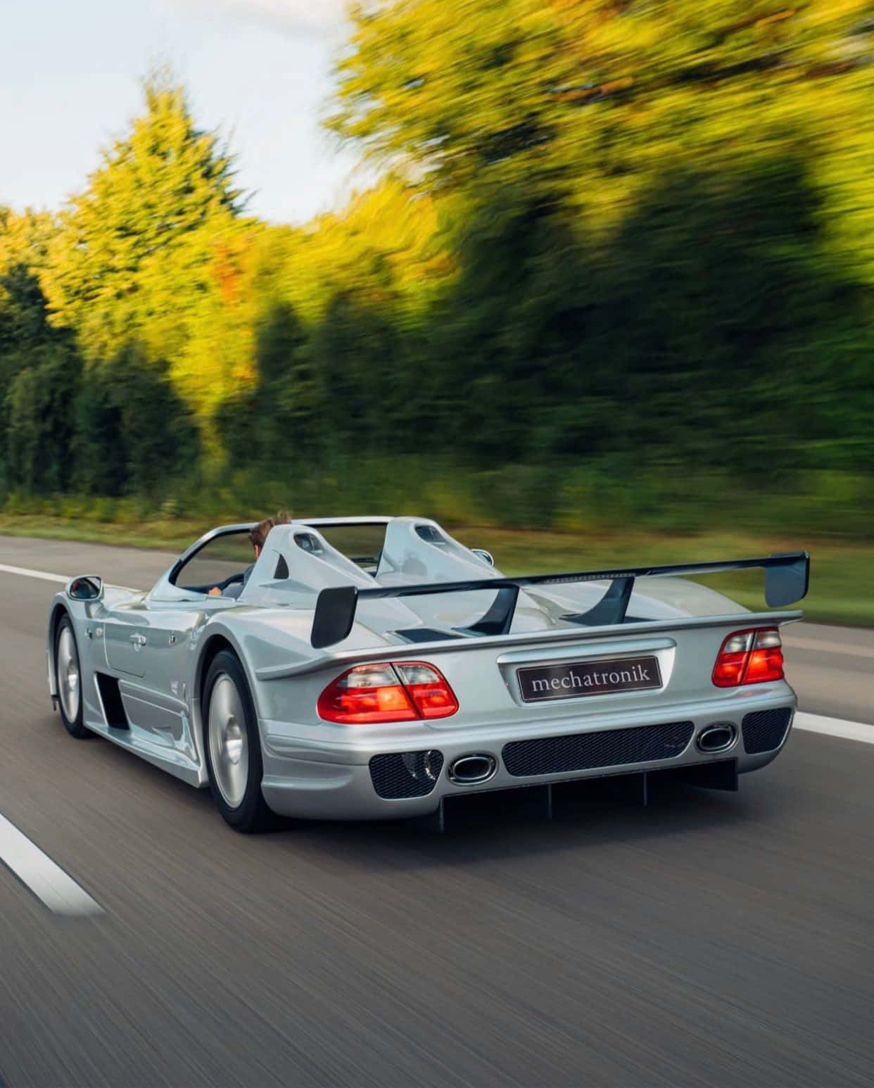 Speed Racer 桌布 壁紙 — 一輛銀色 Mercedes-Benz CLK GTR Mechatronik 在樹林環繞的道路上疾馳，動態模糊強調了速度。