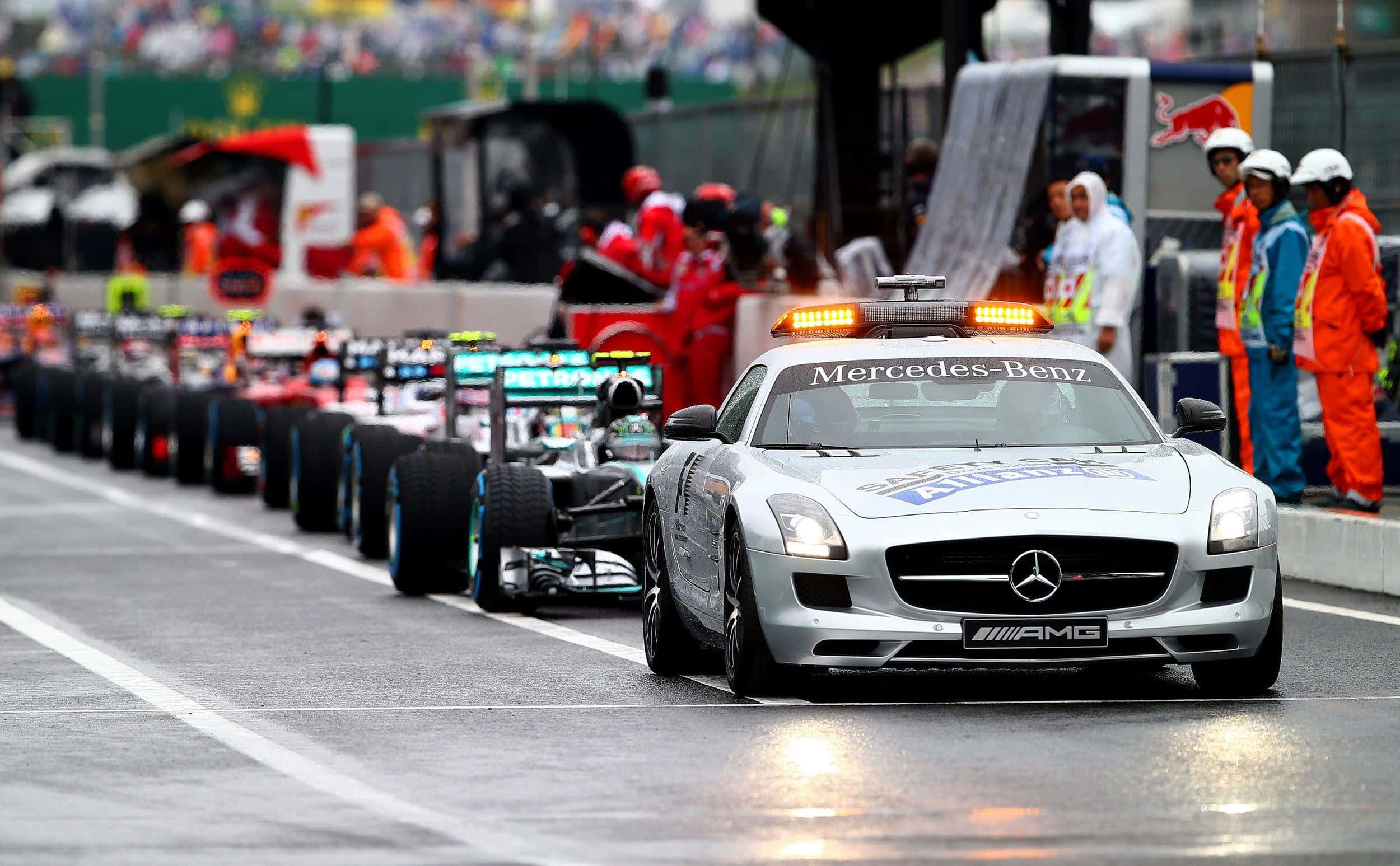 Safety Car 桌布 壁紙 — 一輛銀色 Mercedes-Benz 安全車帶領一排 Formula 1 賽車在濕滑賽道上行駛，附近有身穿橙色套裝的工作人員。