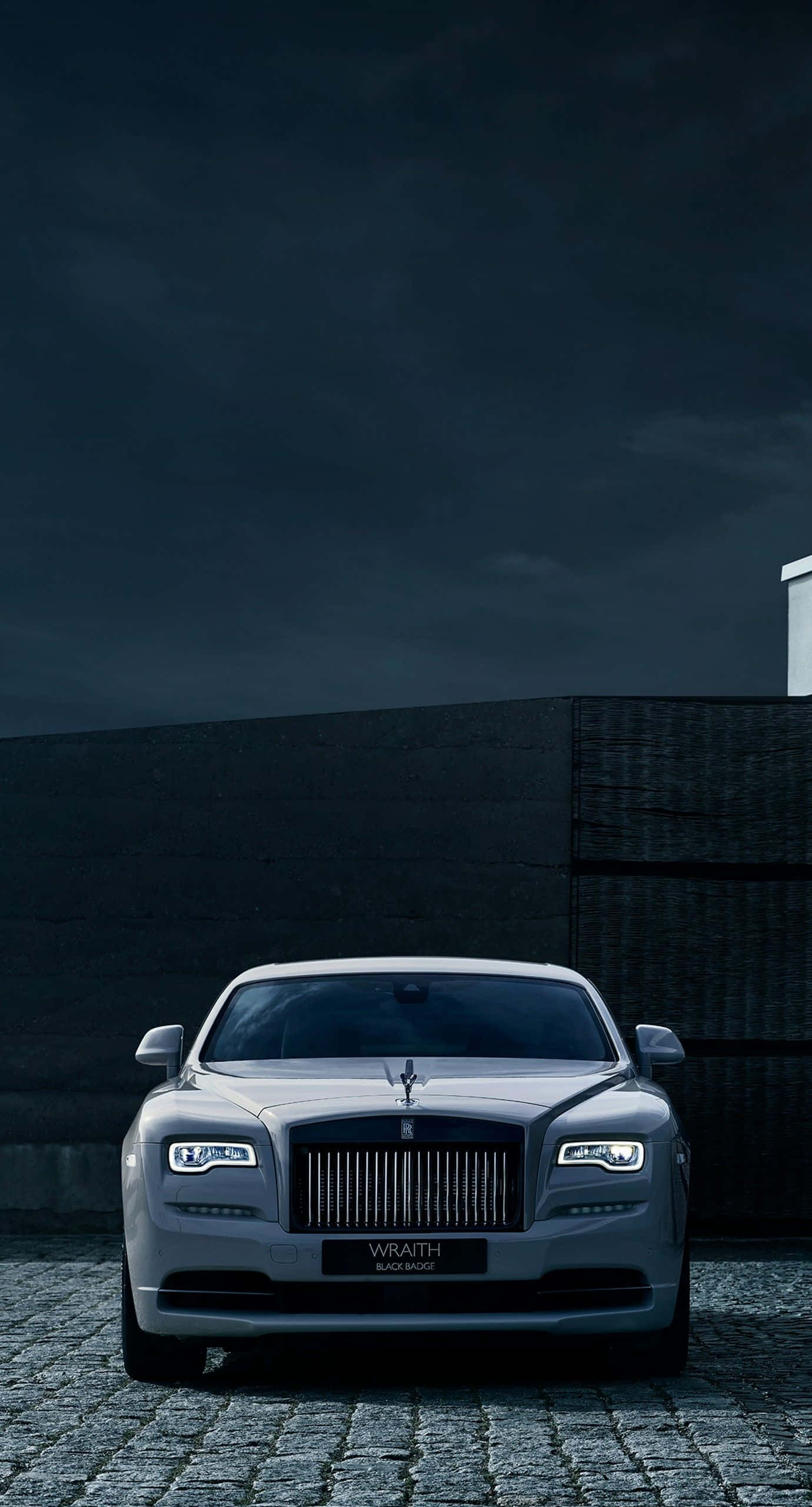 勞斯萊斯 桌布 壁紙 — 一輛銀色 Rolls Royce Wraith Black Badge 在暴風雨的夜空下，在鵝卵石街道上閃閃發光。