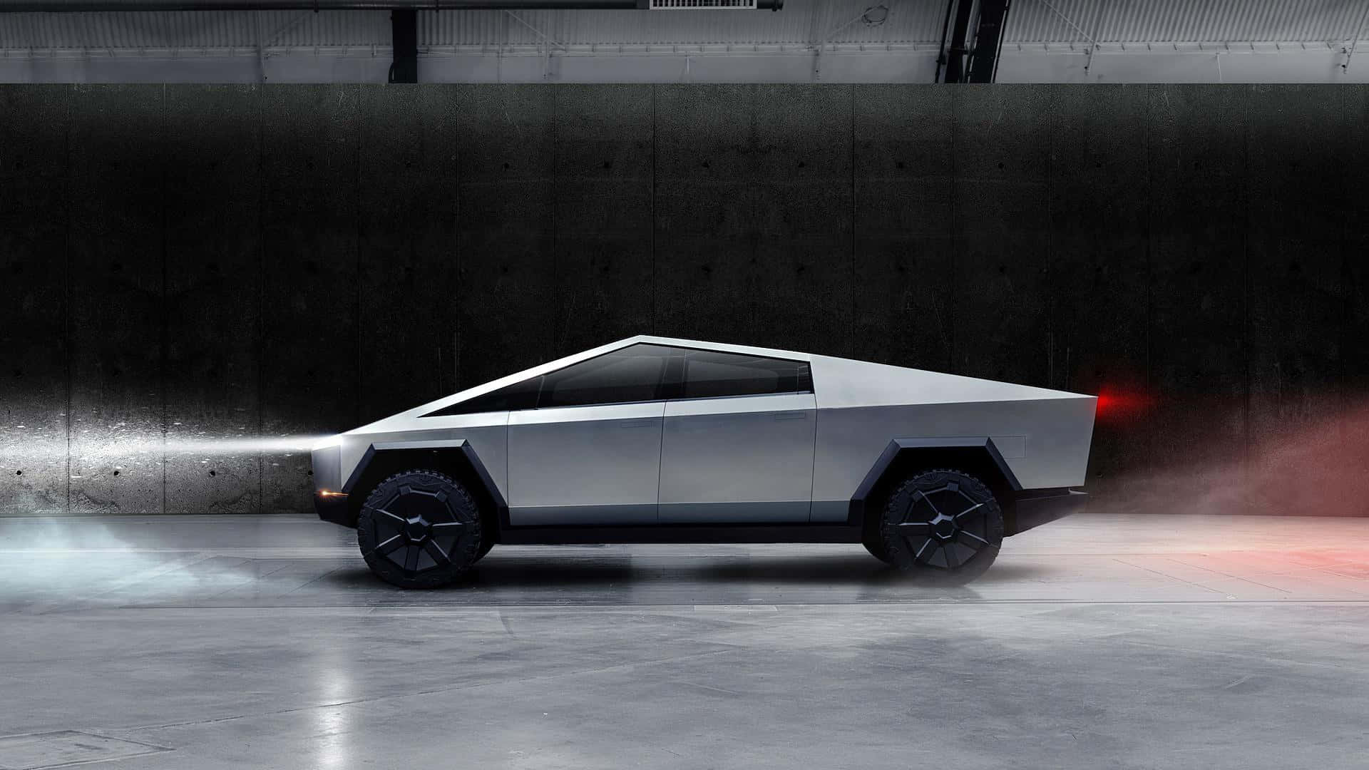 Tesla Cybertruck 桌布 壁紙 — 一輛銀色 Tesla Cybertruck，線條銳利方正，車頭燈發光，停放在昏暗的混凝土車庫中，車尾有紅色煙霧裊裊升起。