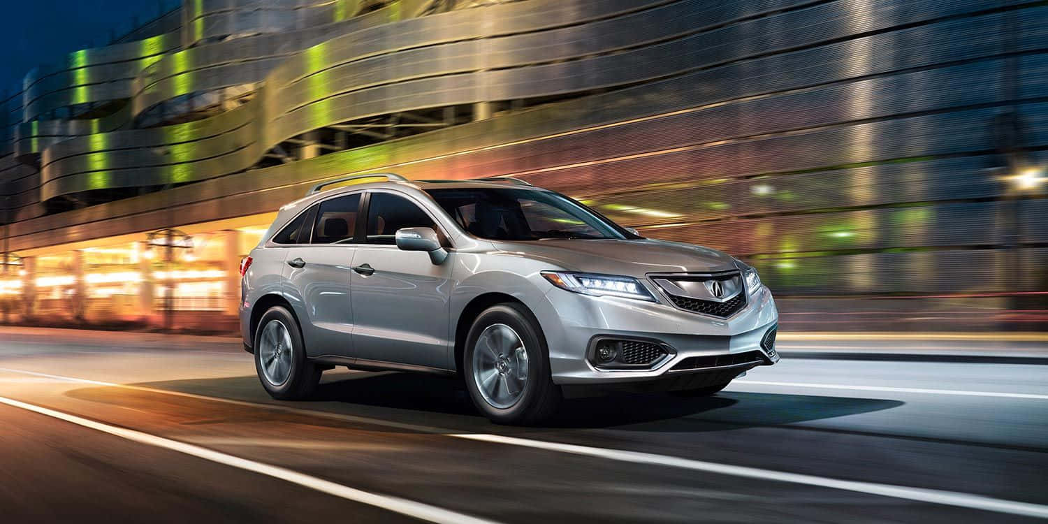 Acura Rdx 桌布 壁紙 — 一輛銀色Acura SUV在夜間穿越充滿活力的城市景觀，帶有動態模糊效果。