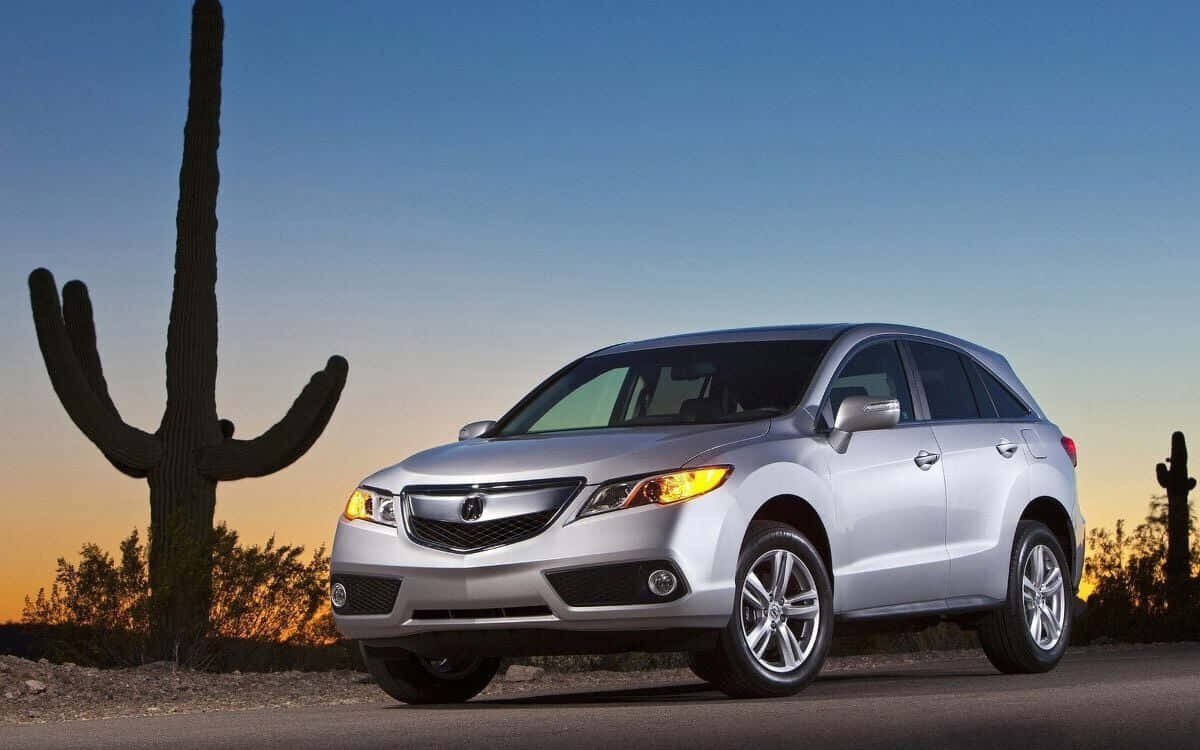 Acura Rdx 桌布 壁紙 — 一輛銀色Acura SUV在日落時停泊在沙漠公路旁，旁邊有一棵高大的薩瓜羅仙人掌。