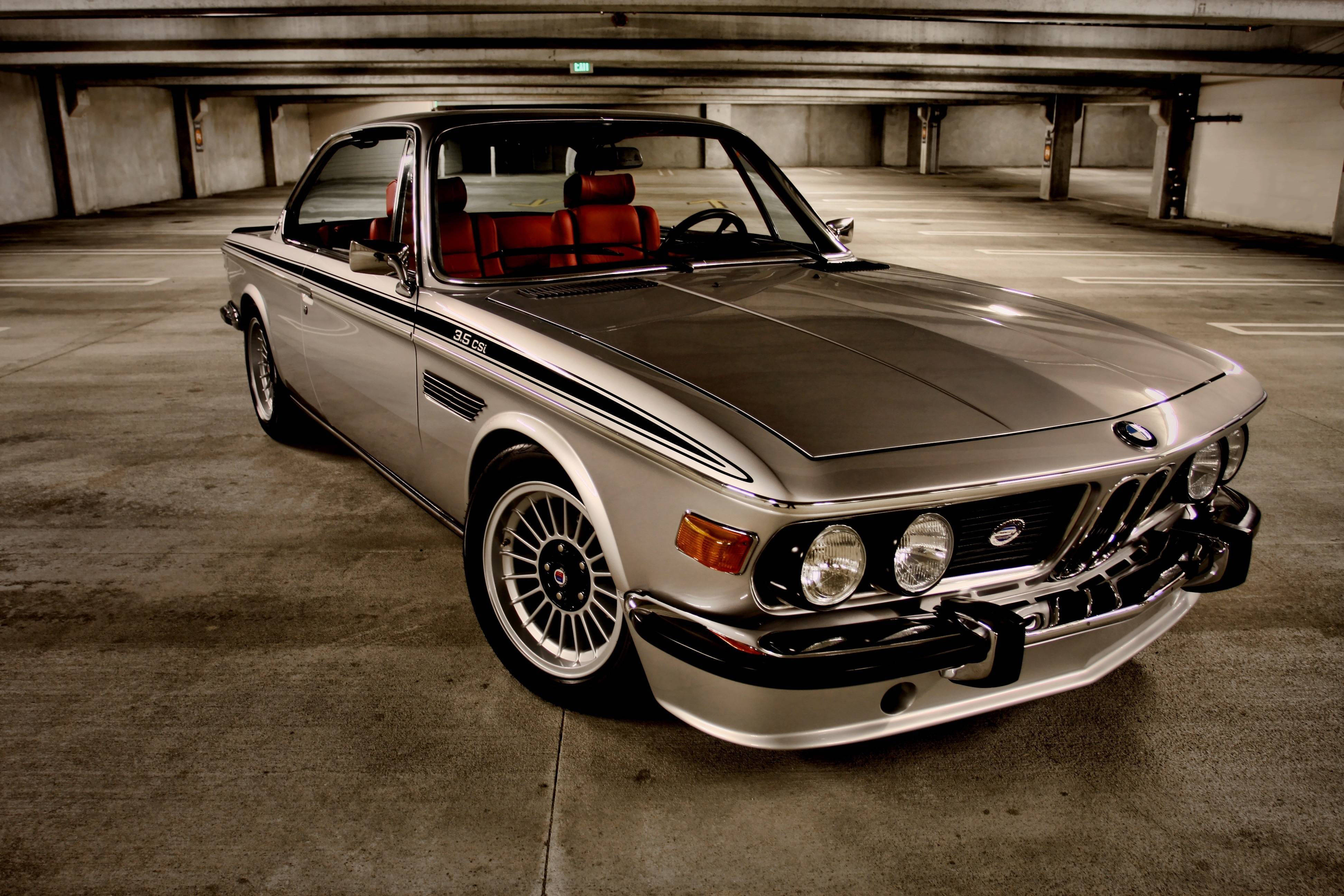 classic bmw 桌布 壁紙 — 一輛銀色BMW 3.0 CSL配紅色內裝停放在光線昏暗的混凝土停車場。