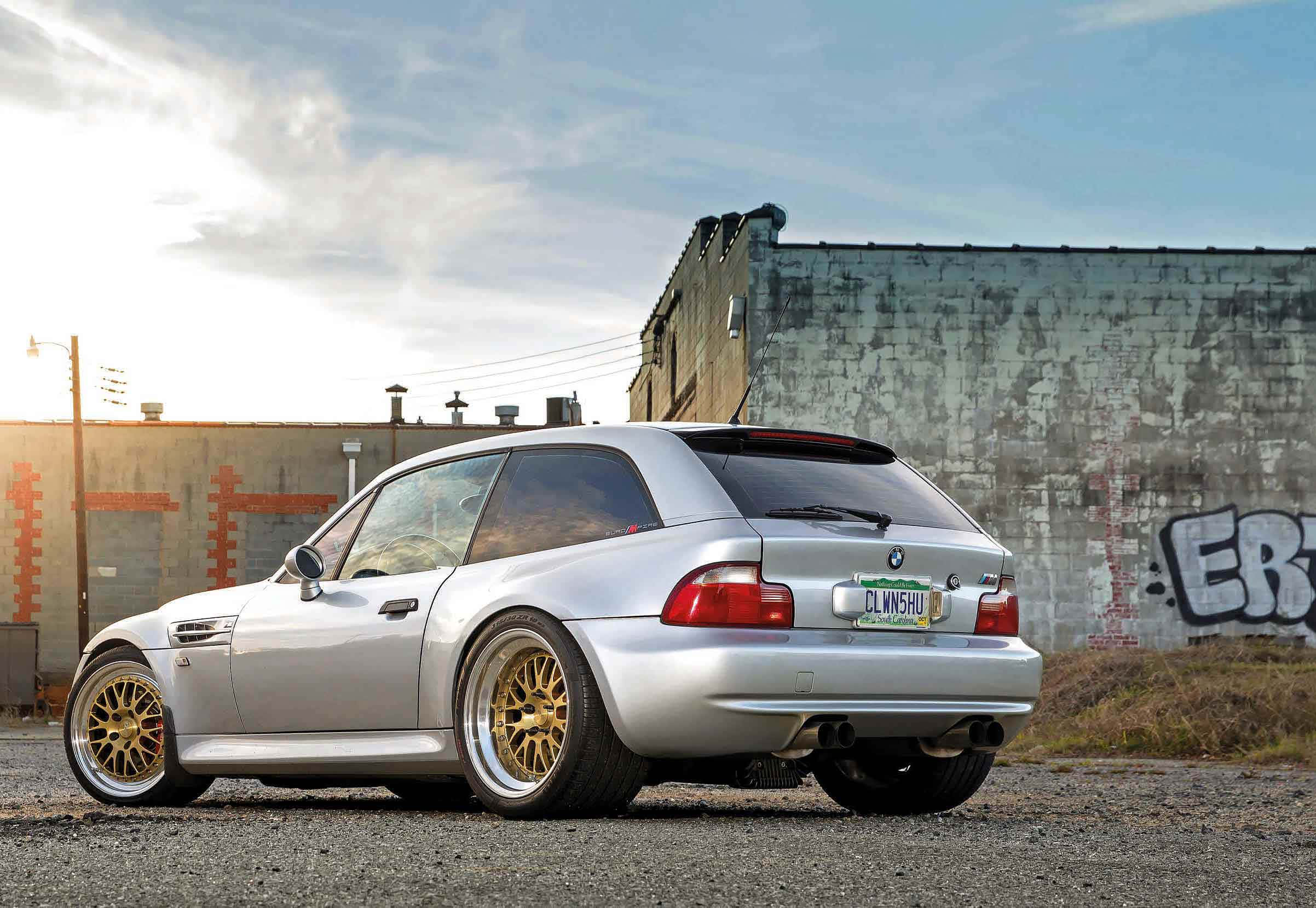 Bmw Z3 桌布 壁紙 — 一輛銀色BMW M3配金色輪圈，在日落時停泊在碎石上，旁邊是佈滿塗鴉的工業牆。
