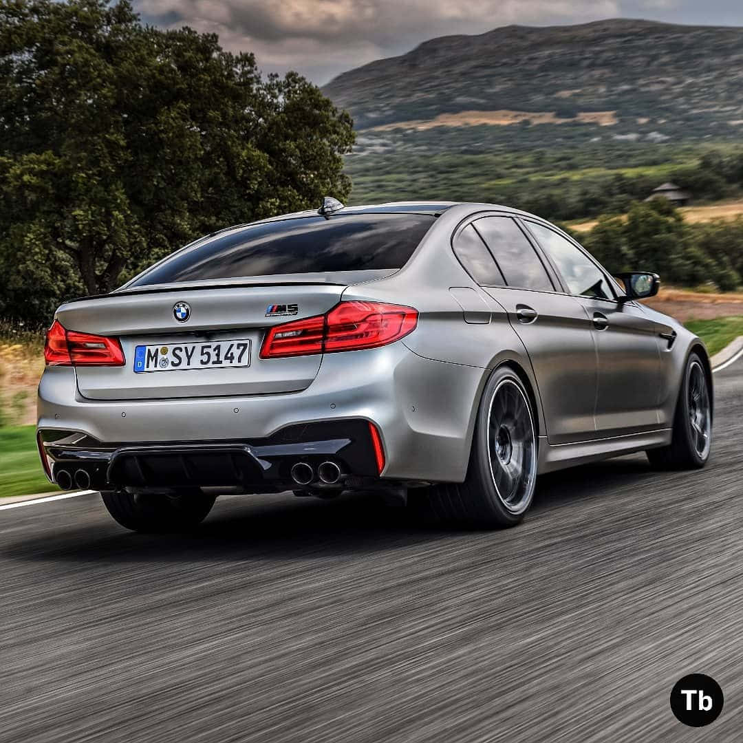 speeding car 桌布 壁紙 — 一輛銀色BMW M5轎車在陰天之下，沿著蜿蜒的道路穿過翠綠的鄉間飛馳。