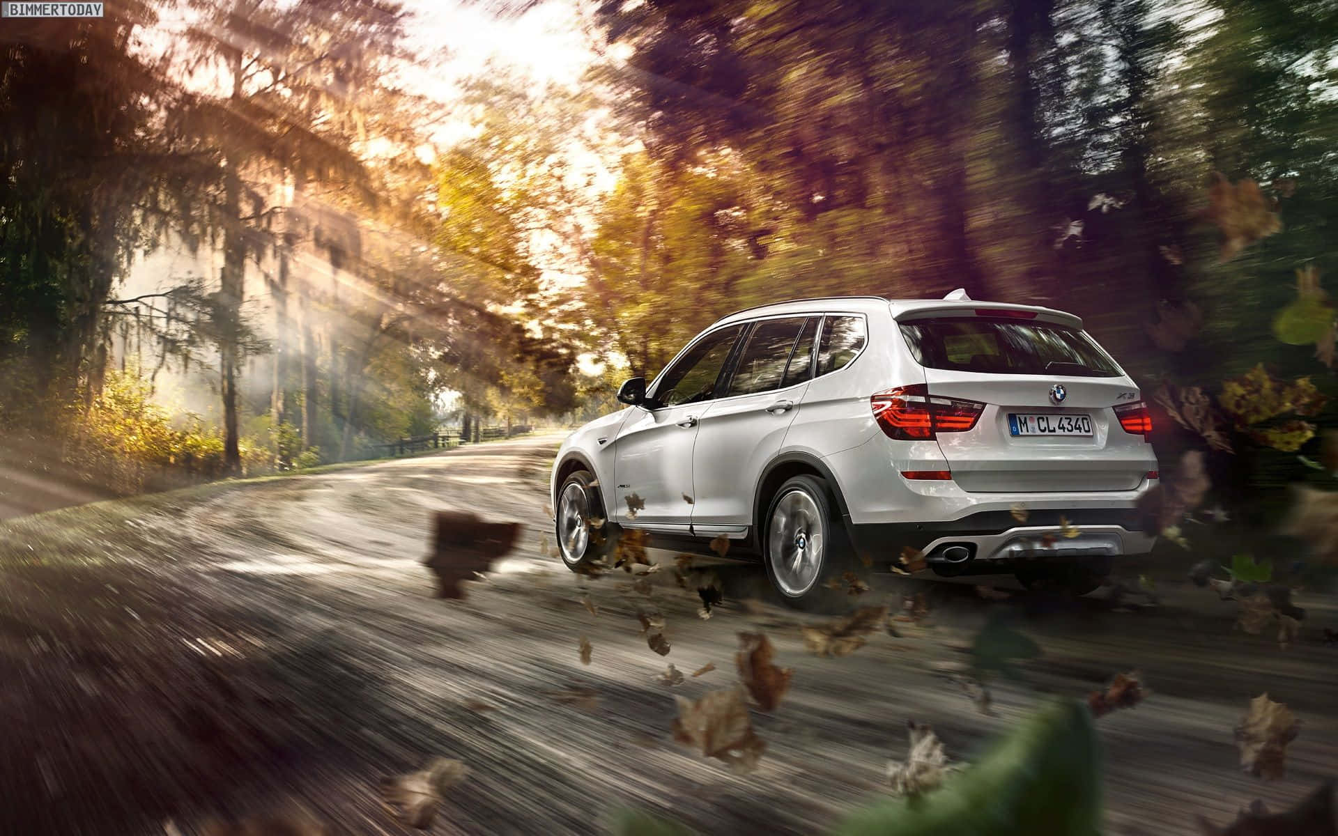 Bmw X3 桌布 壁紙 — 一輛銀色BMW SUV在陽光明媚的秋日森林中疾馳，落葉在車輪周圍旋轉。