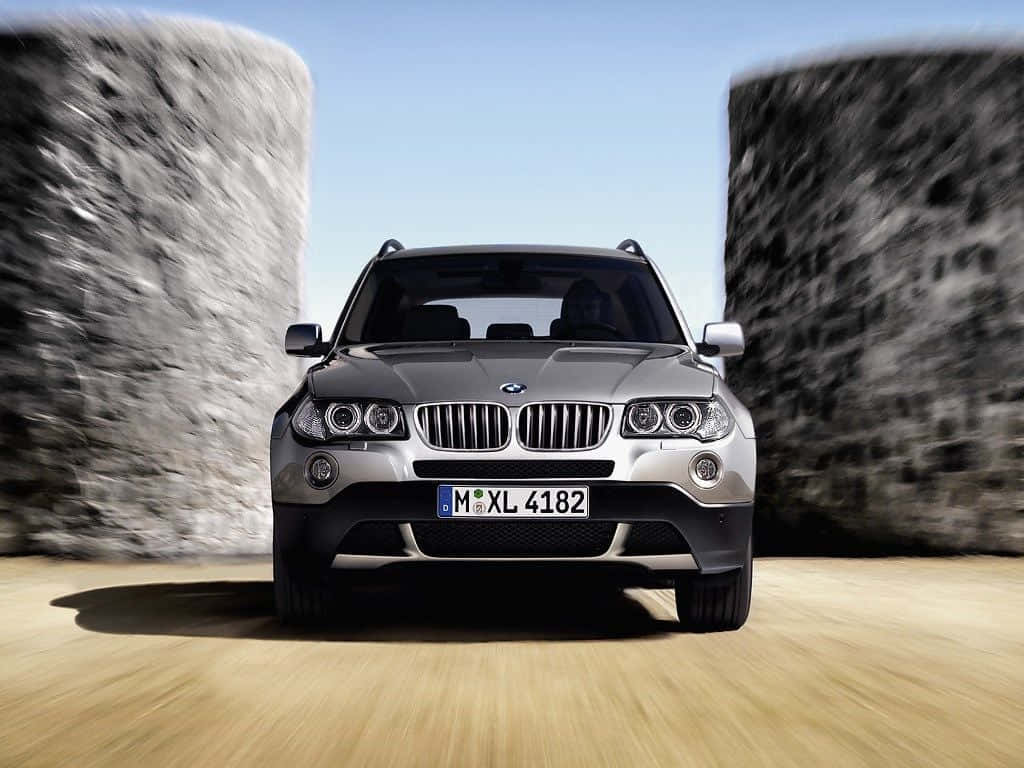 Bmw X3 桌布 壁紙 — 一輛銀色BMW X5 SUV在石牆和木地板上，於晴朗藍天下帶著動態模糊向前飛馳。