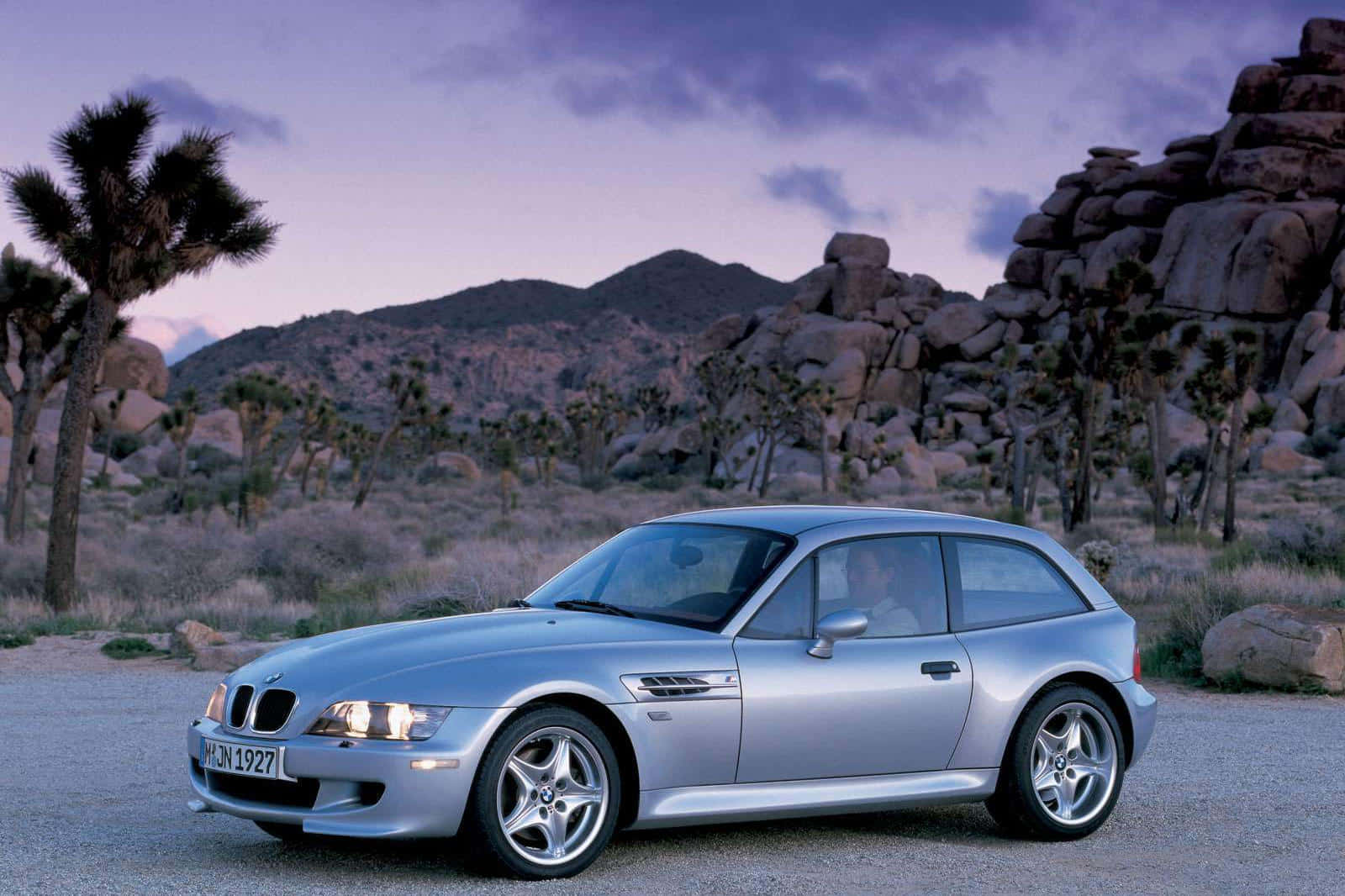 Bmw Z3 桌布 壁紙 — 一輛銀色BMW Z3敞篷跑車停泊在暮色中的沙漠碎石路上，背景有約書亞樹和岩石山丘。