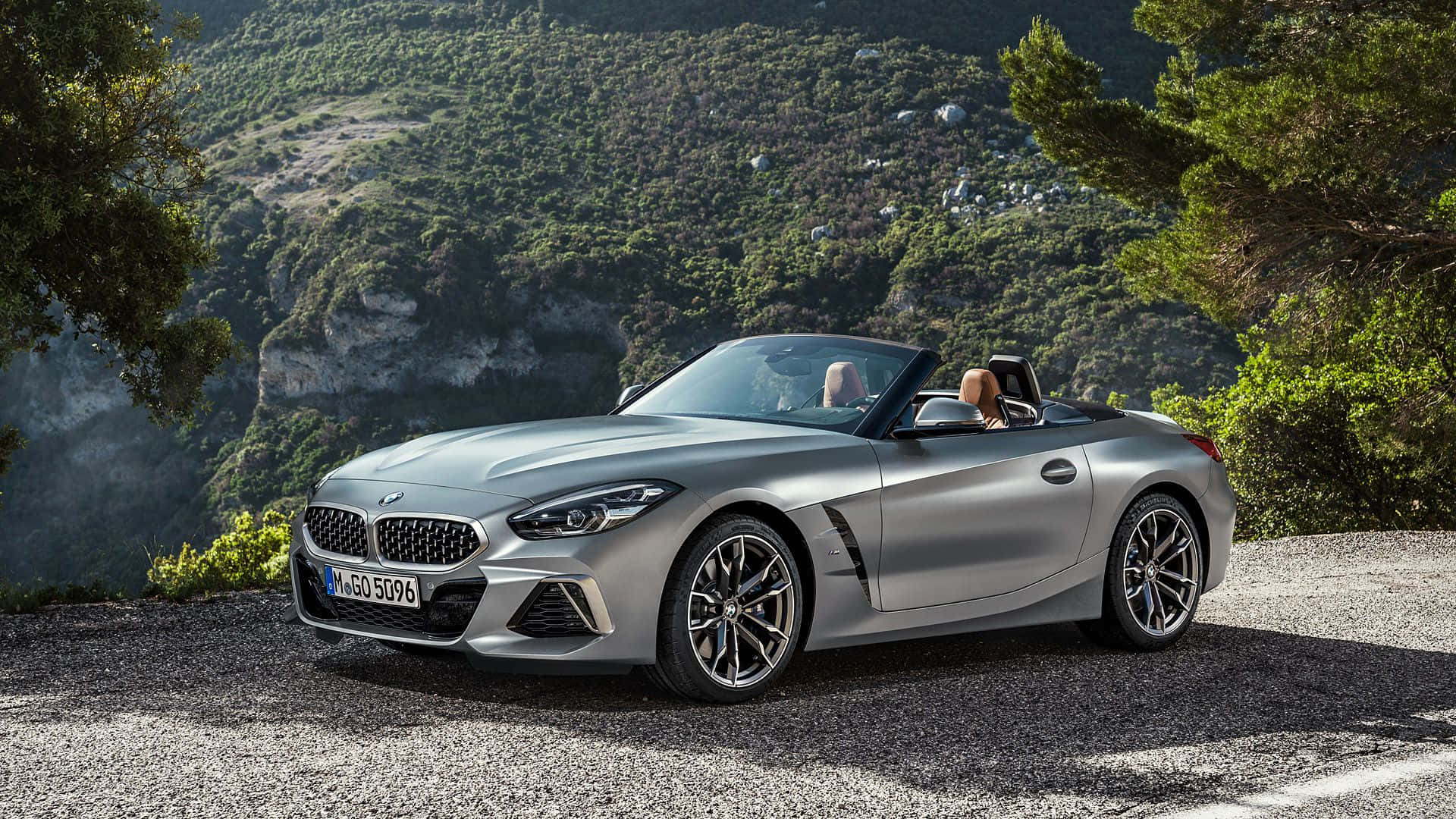 Bmw Z4 桌布 壁紙 — 一輛銀色BMW Z4敞篷車停在碎石路上，兩個人正在欣賞風景如畫的山景。