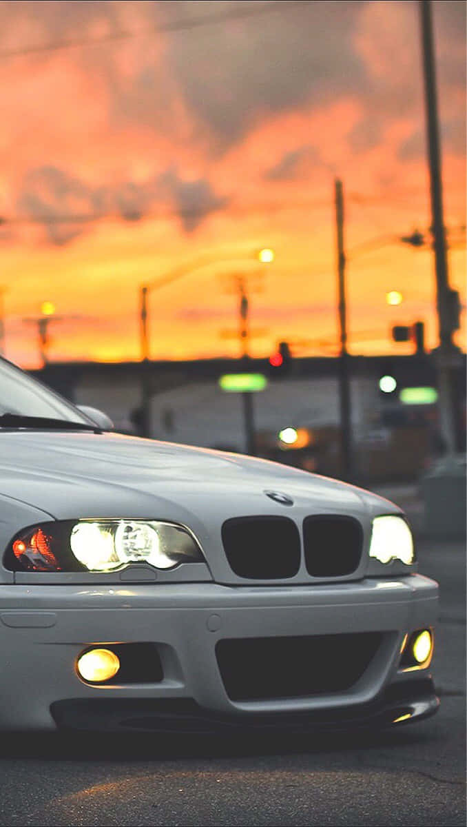 Bmw Android 桌布 壁紙 — 一輛銀色BMW跑車在火紅橙色的夕陽天空下閃耀，背景是模糊的城市燈光。