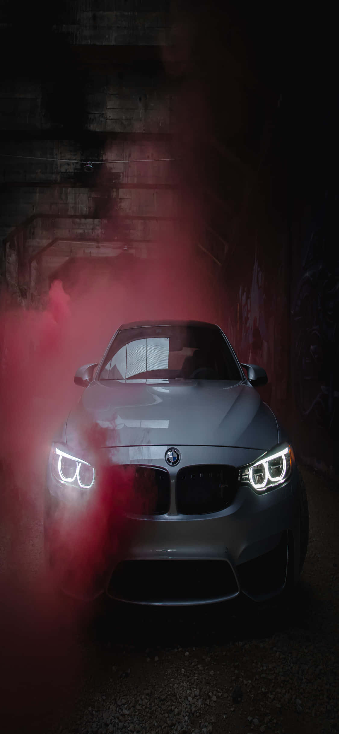 iPhone X Bmw 桌布 壁紙 — 一輛銀色BMW跑車在黑暗的混凝土隧道中從紅煙中出現，車頭燈發光。