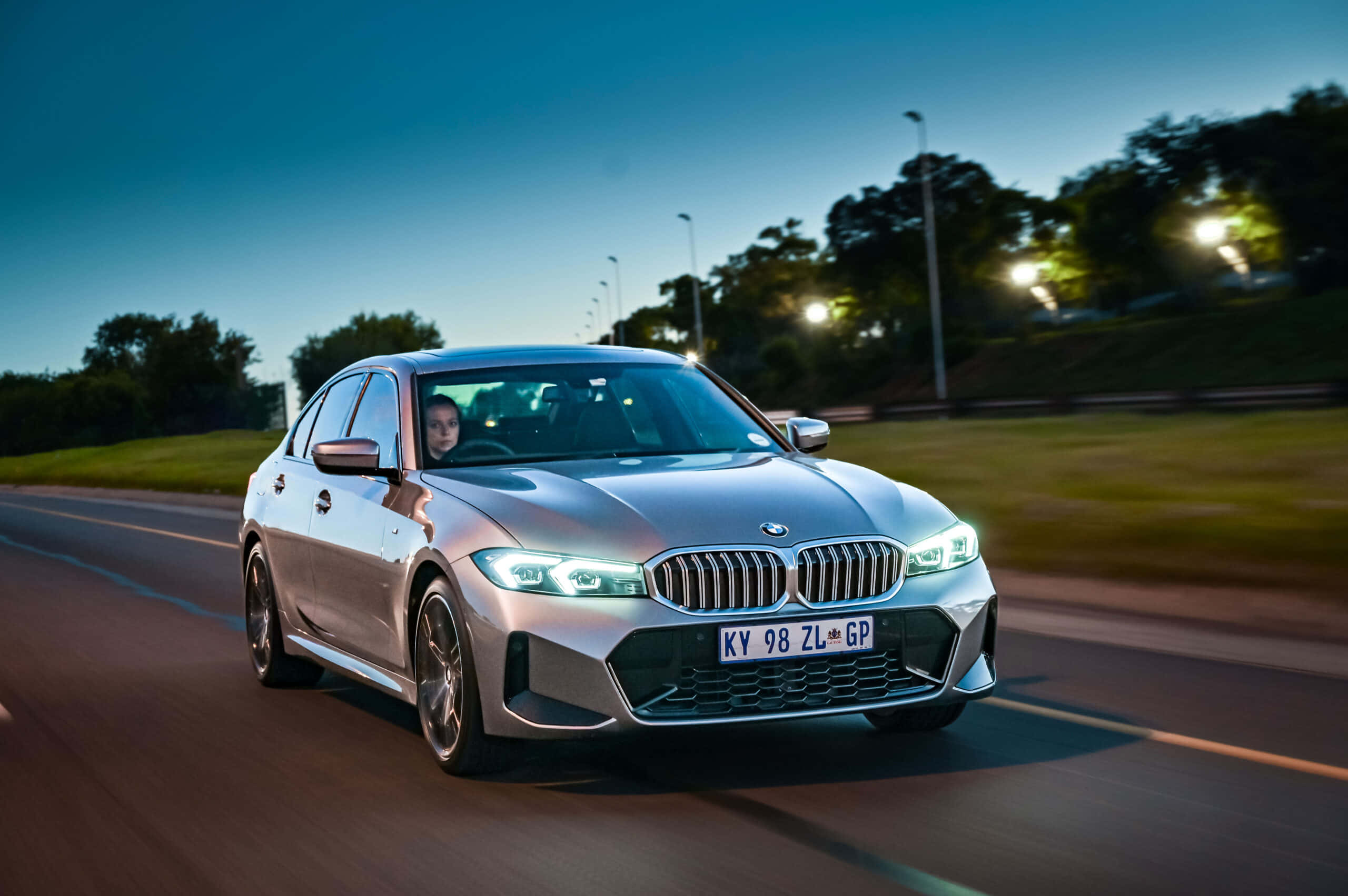 Bmw 3 Series 桌布 壁紙 — 一輛銀色BMW轎車在暮色道路上疾馳，車頭燈閃爍，周圍模糊。