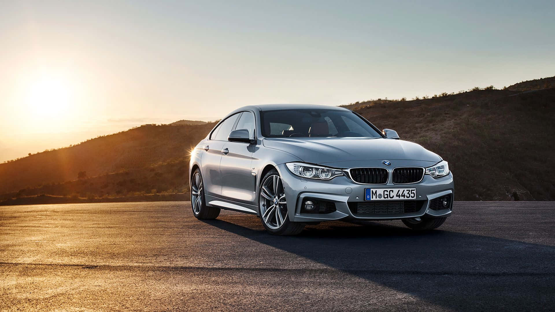 Bmw 4 Series 桌布 壁紙 — 一輛銀色BMW轎車在金色夕陽下，於沙漠公路上閃耀，背景是起伏的山丘。