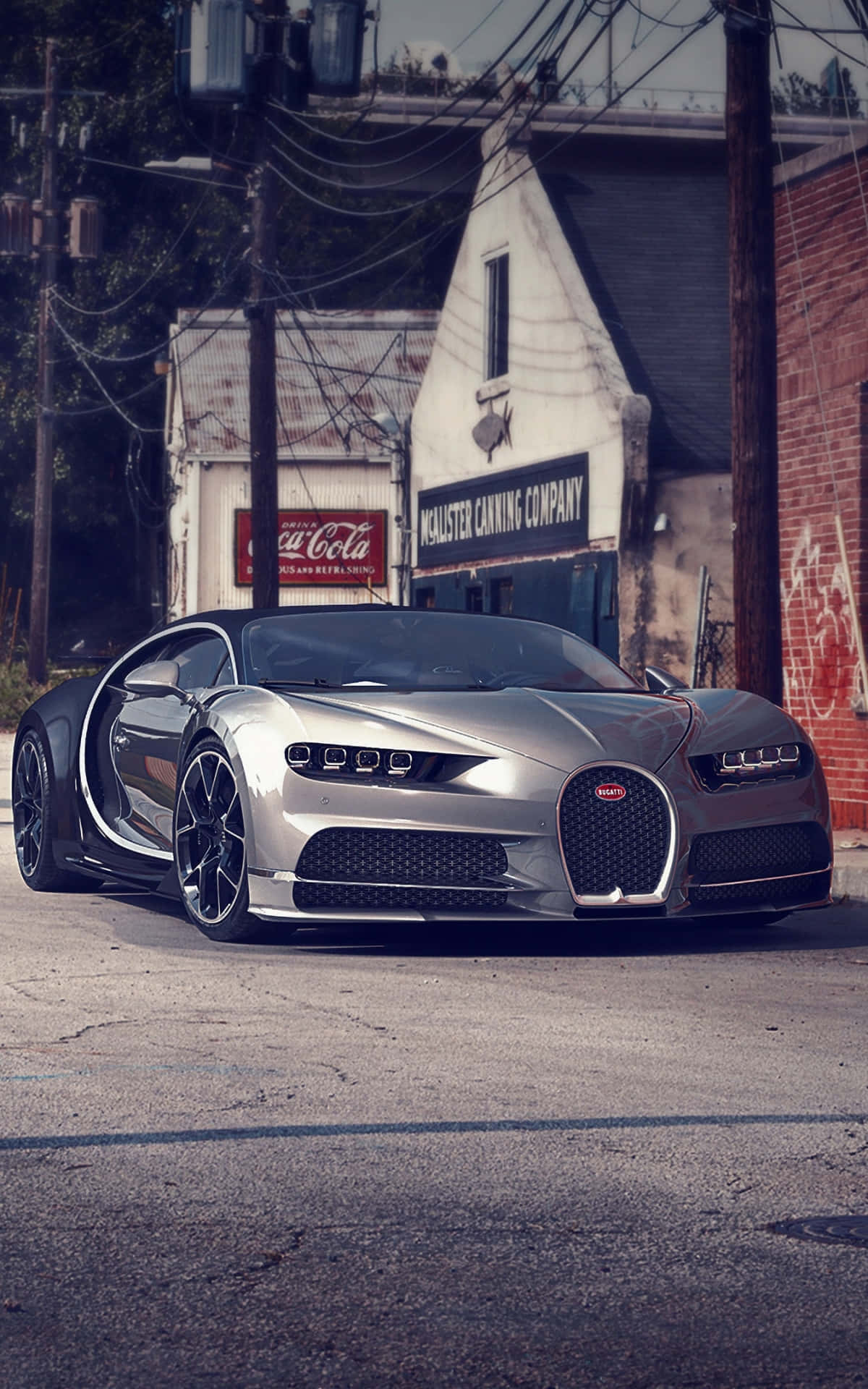 Bugatti Phone 桌布 壁紙 — 一輛銀色Bugatti Chiron打開車門，停在裂開的柏油路面上，前方是帶有褪色招牌的復古磚造建築。