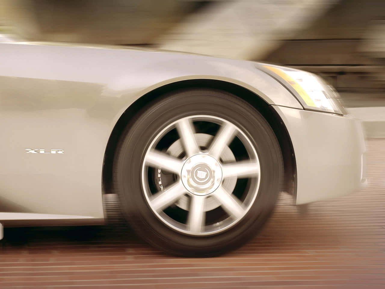 Cadillac Xlr 桌布 壁紙 — 一輛銀色Cadillac XLR跑車高速駛過，動態模糊凸顯其流線型設計和旋轉的車輪。