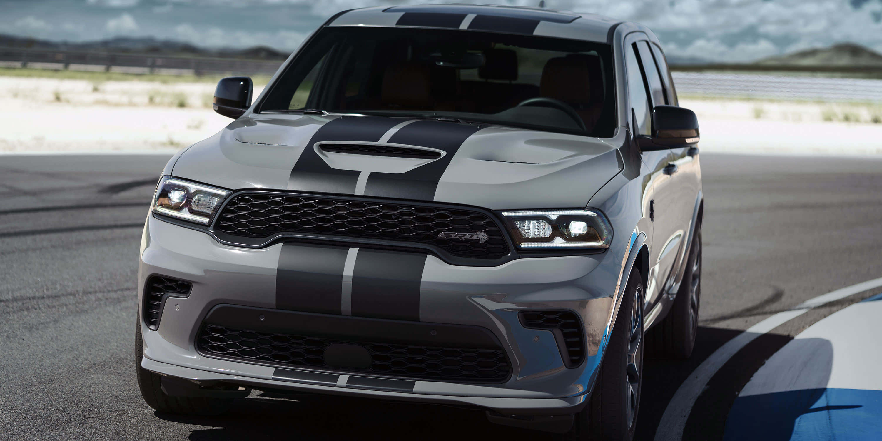 Dodge 桌布 壁紙 — 一輛銀色Dodge Durango SRT帶有黑色賽車條紋，在陰天下的賽道上蓄勢待發。