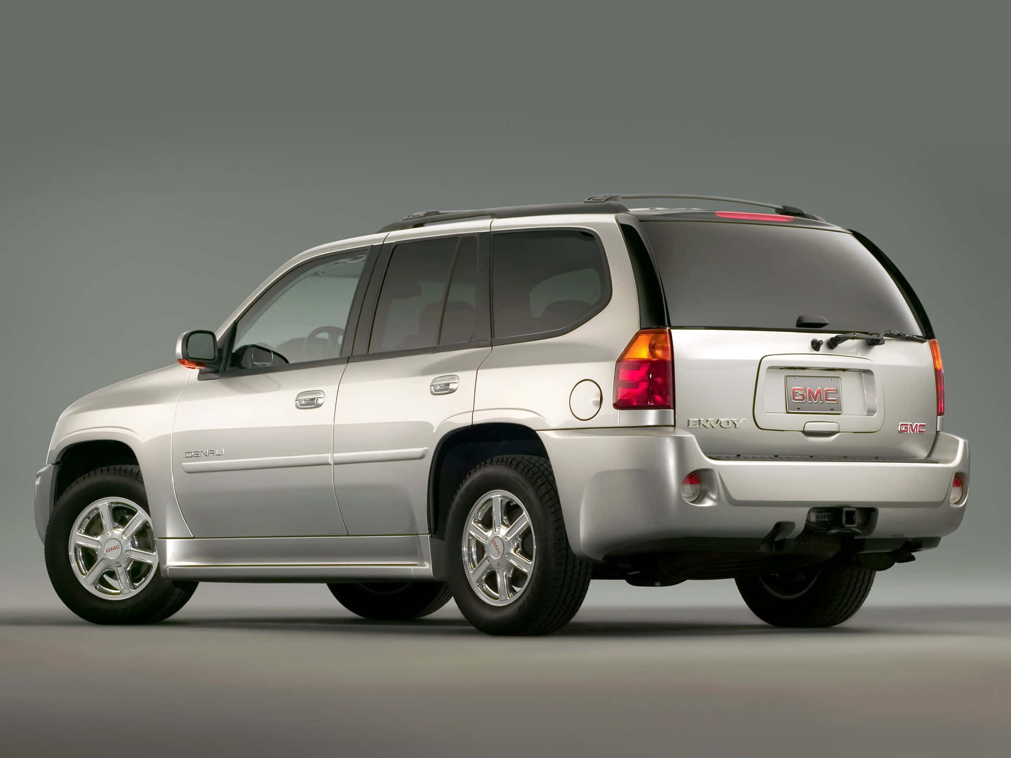 Gmc Envoy 桌布 壁紙 — 一輛銀色GMC Envoy SUV以四分之三後視圖展示，背景為中性灰色攝影棚。
