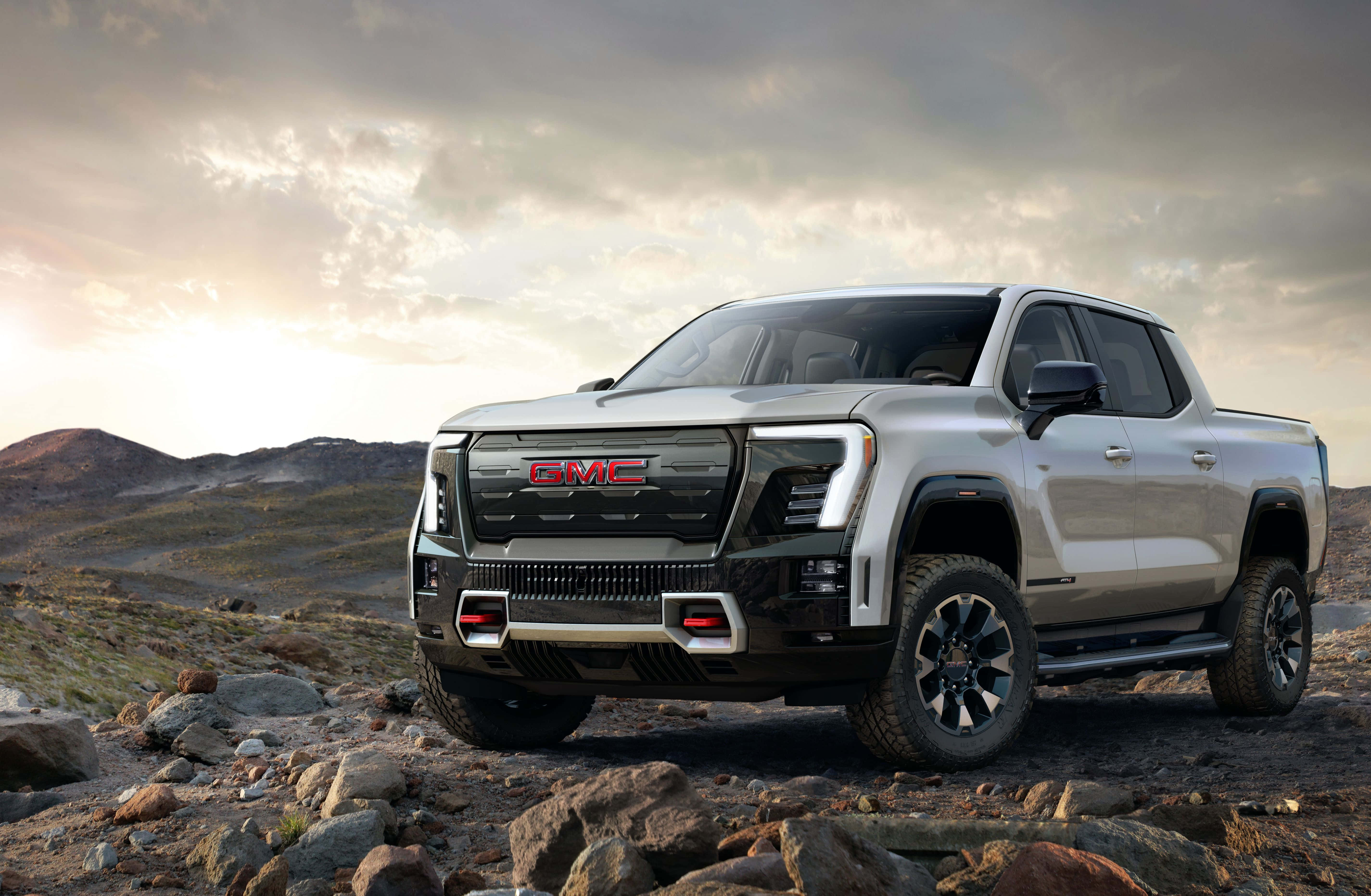Gmc Sierra 桌布 壁紙 — 一輛銀色GMC Sierra AT4 pickup truck在戲劇性的日落天空下，堅固地停在岩石沙漠小徑上。