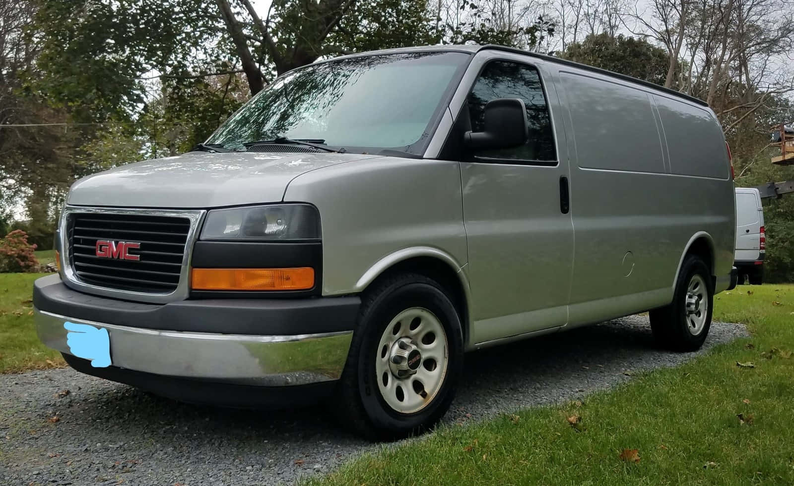Gmc Savana 桌布 壁紙 — 一輛銀色GMC貨車停泊在碎石車道上，周圍是綠草和無葉樹木。
